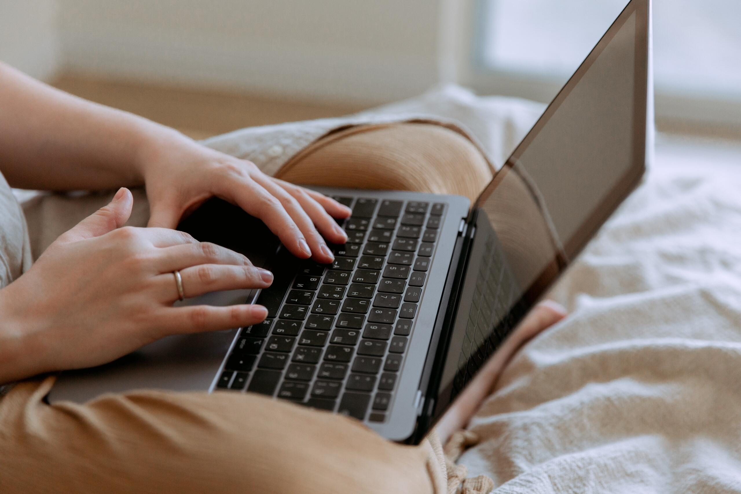 woman sitting on bed typing on laptop keyboard