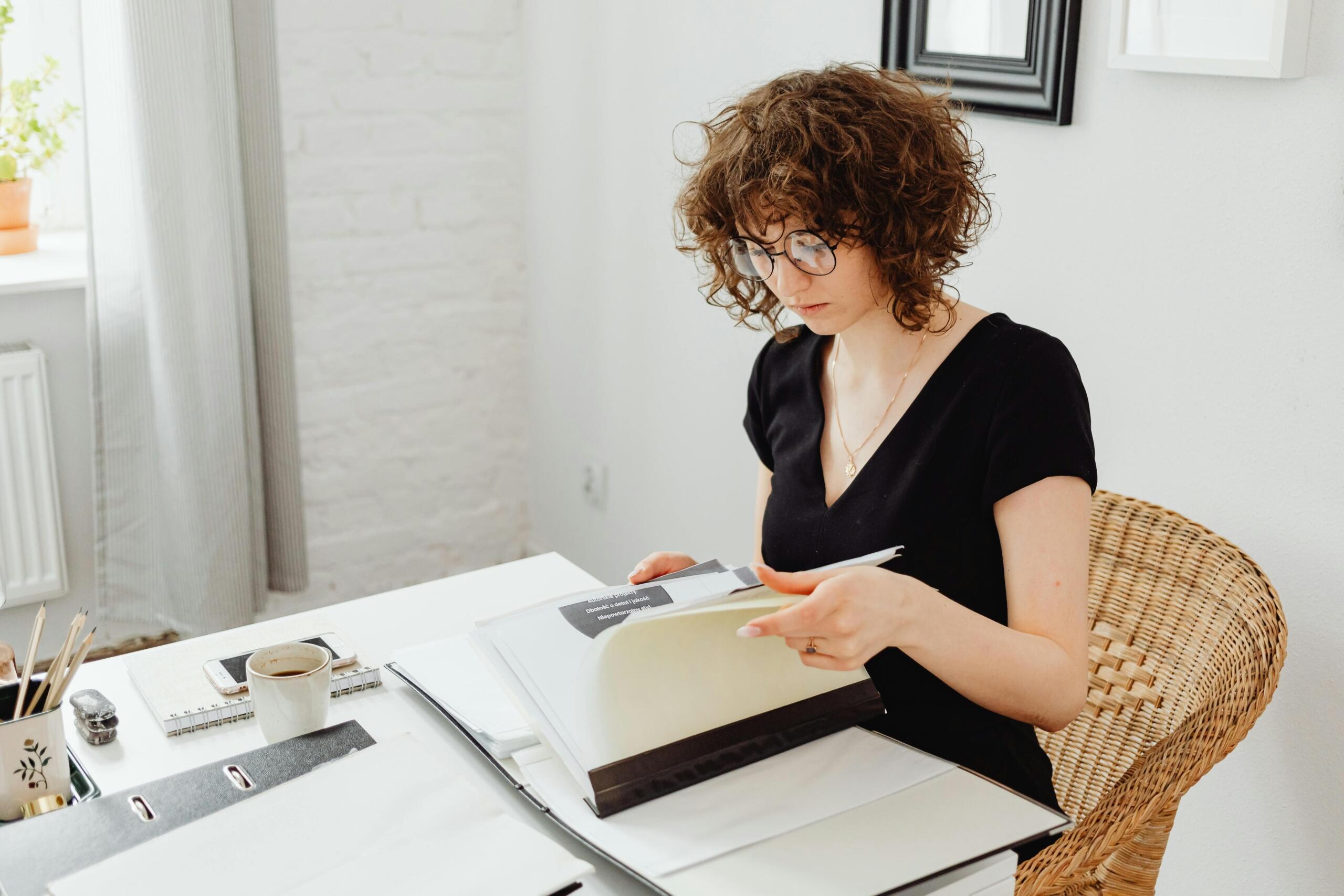 woman seated at a desk with a cup of coffee on it paging through a folder