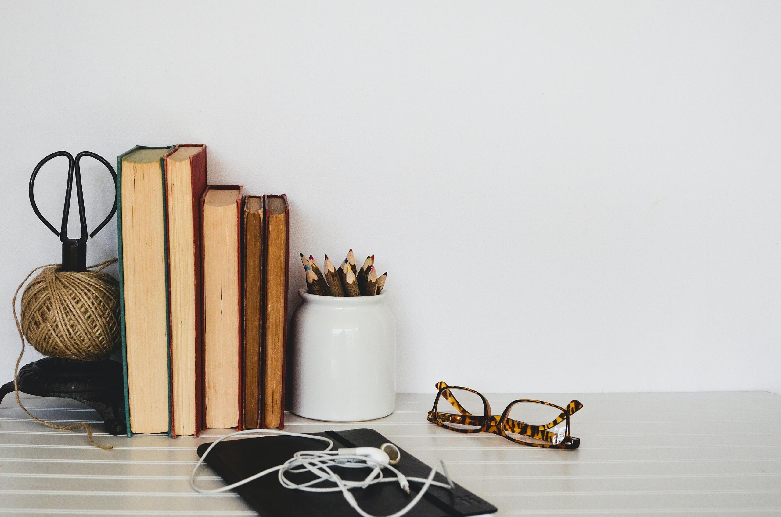 five books placed with their spines against the wall on a desk next to stationery