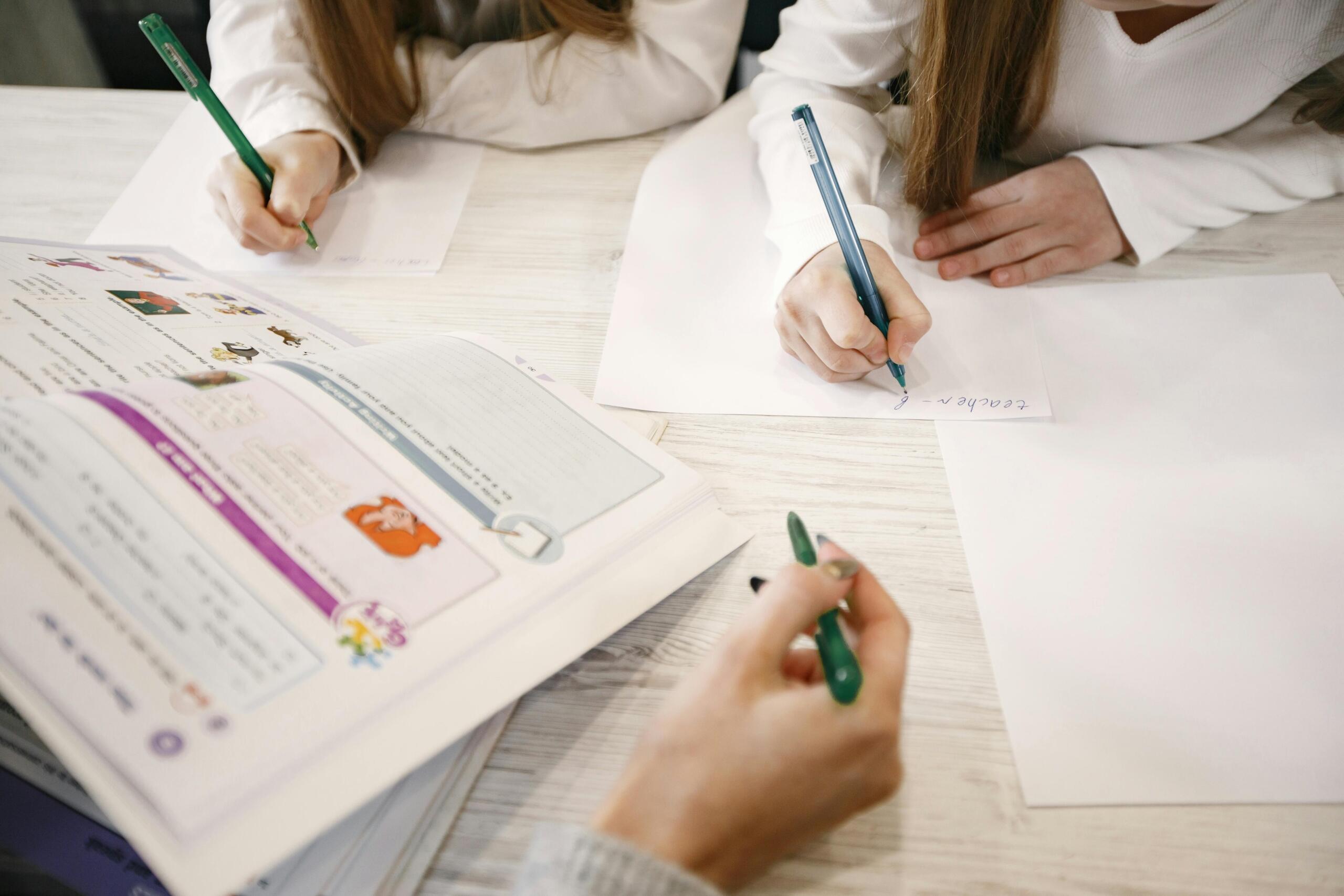 two children sitting at a table doing homework while their mother helps them