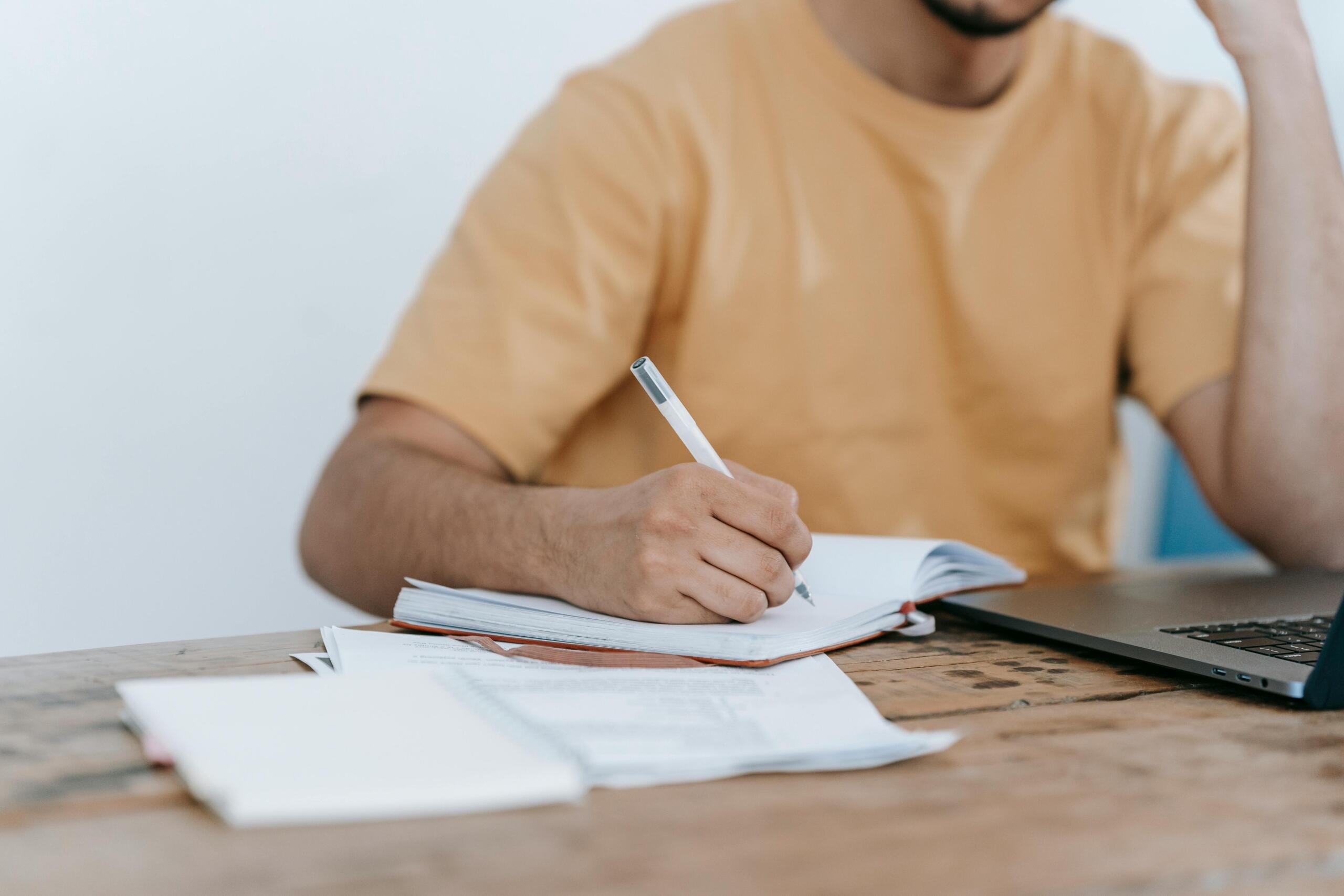 young man using laptop and writing in a notebook