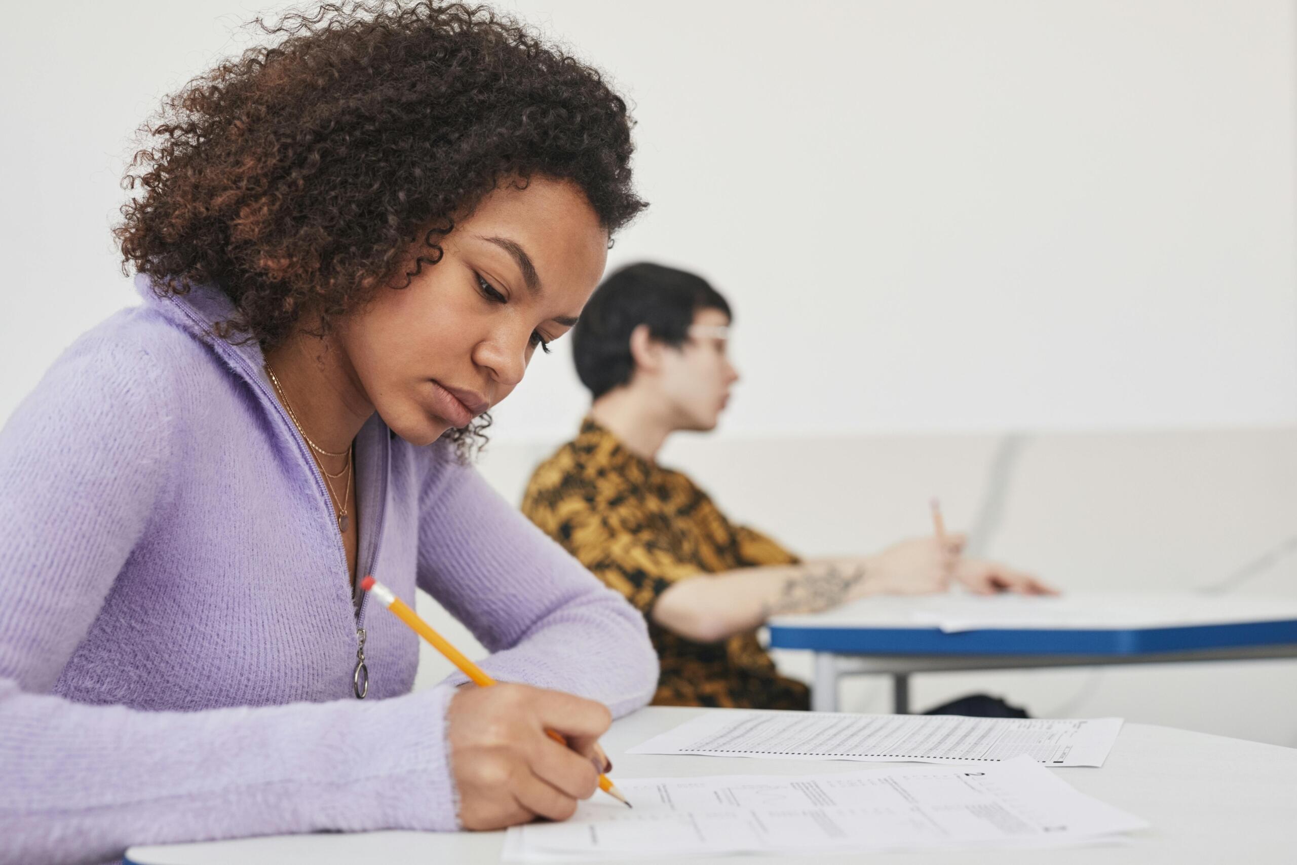 girl in lilac sweater writing an exam using pencil and paper