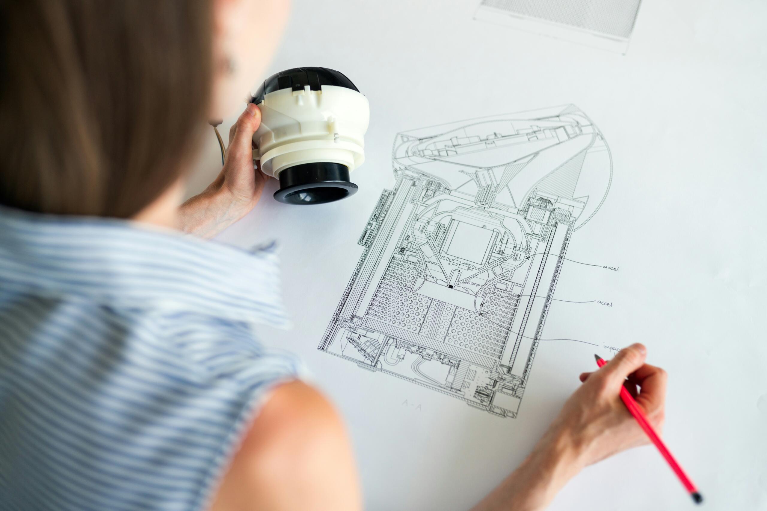 woman drawing an engineering diagram while holding a robot