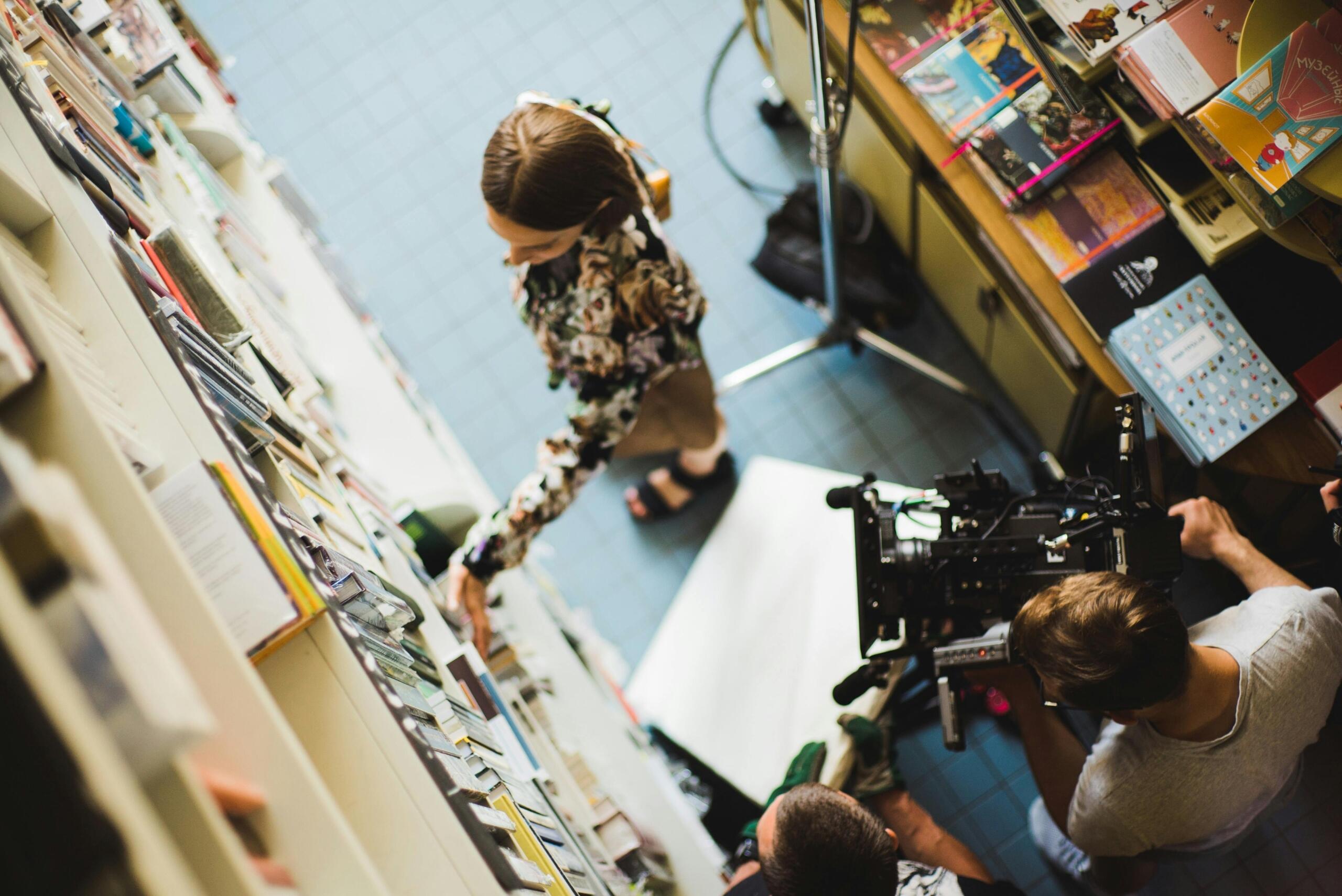 actress in a library reaching for a book on a shelf while being filmed