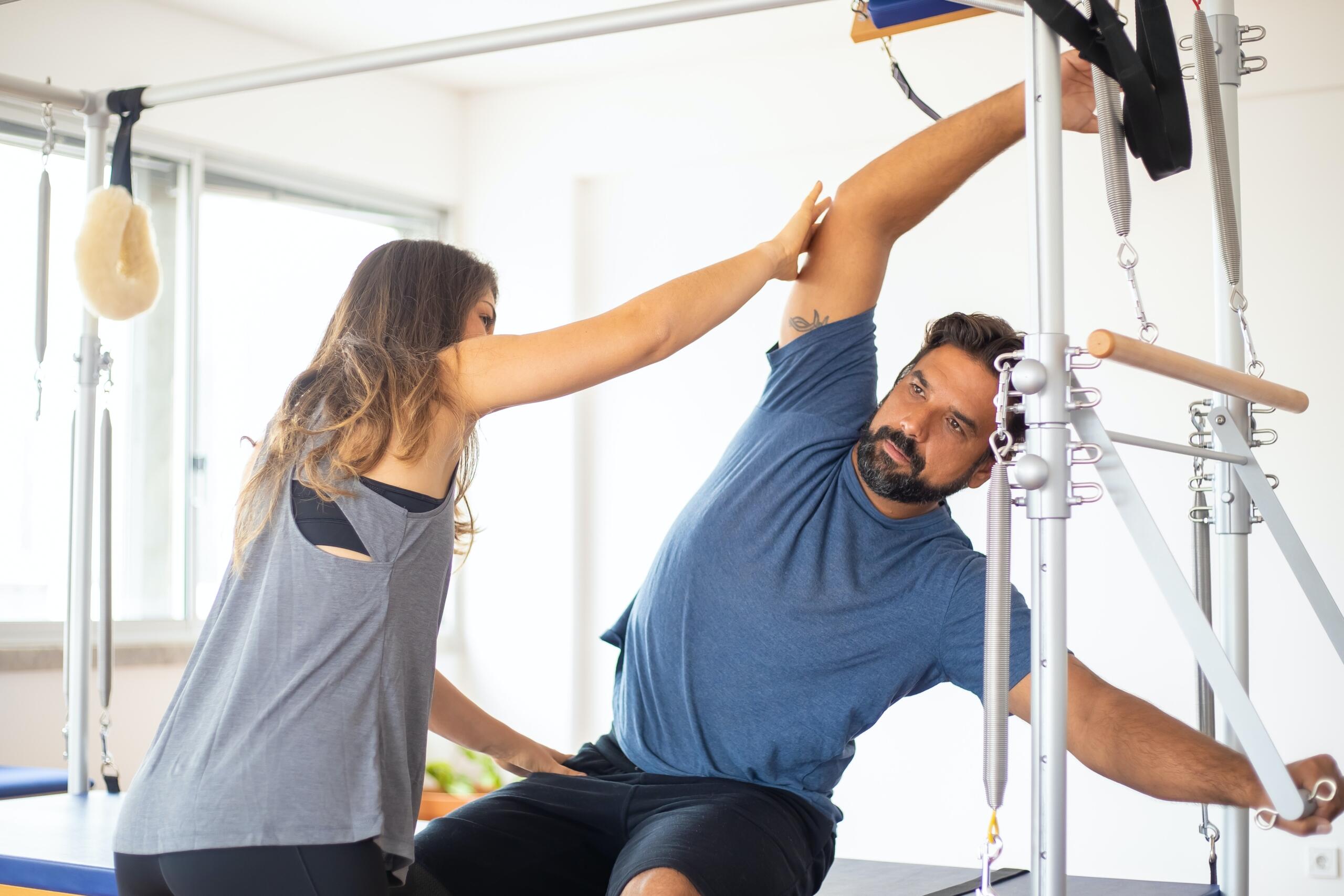 personal trainer helping a man on a pilates reformer machine
