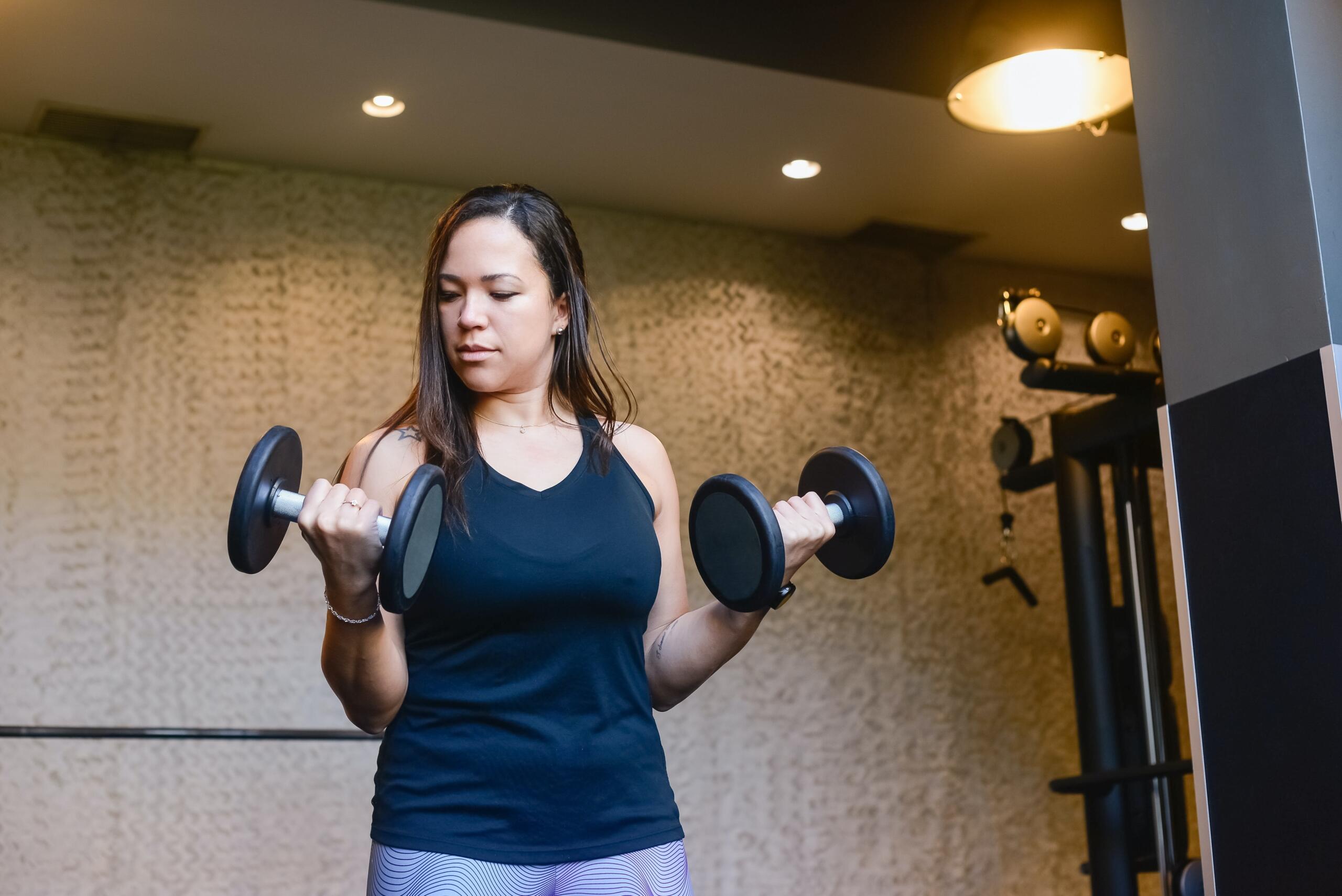 a woman in a gym holding black dumbbells in each hand