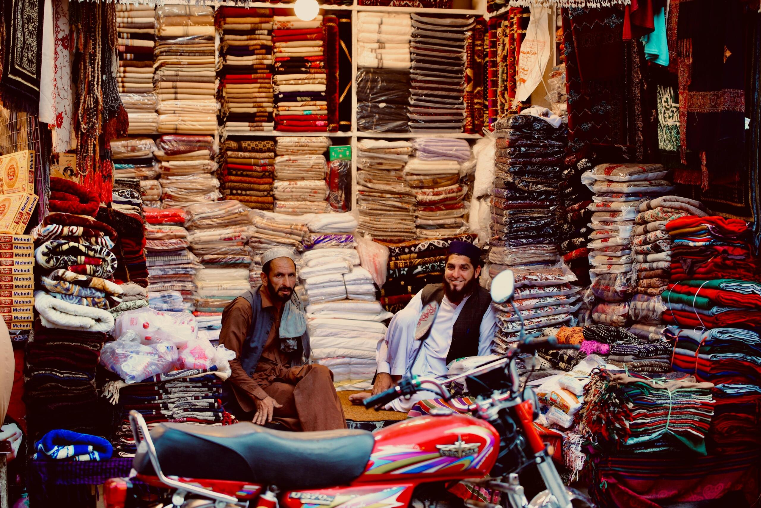 fabric stall in a market with different materials piled high all around the two salesmen