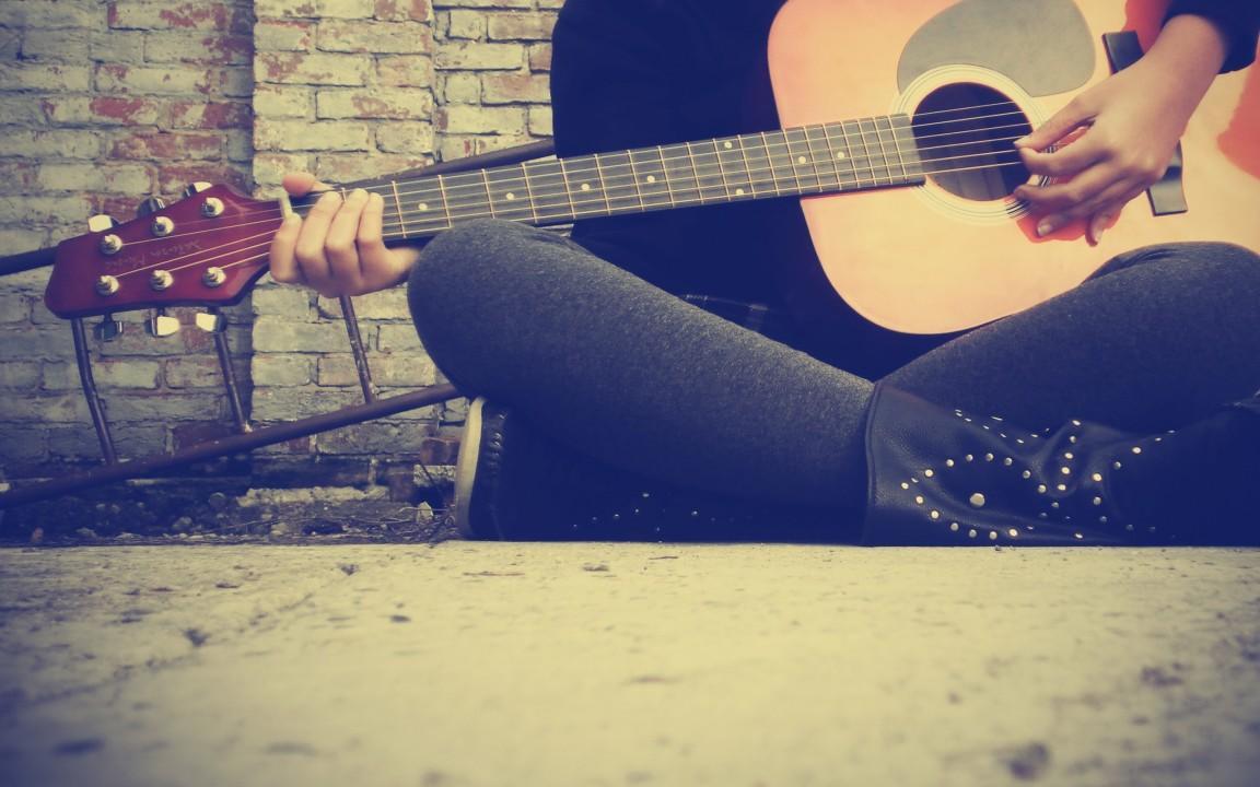 Someone sitting on the floor with a guitar.