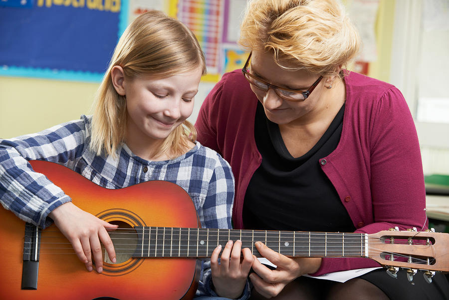 A woman teaching a young girl to play guitar.