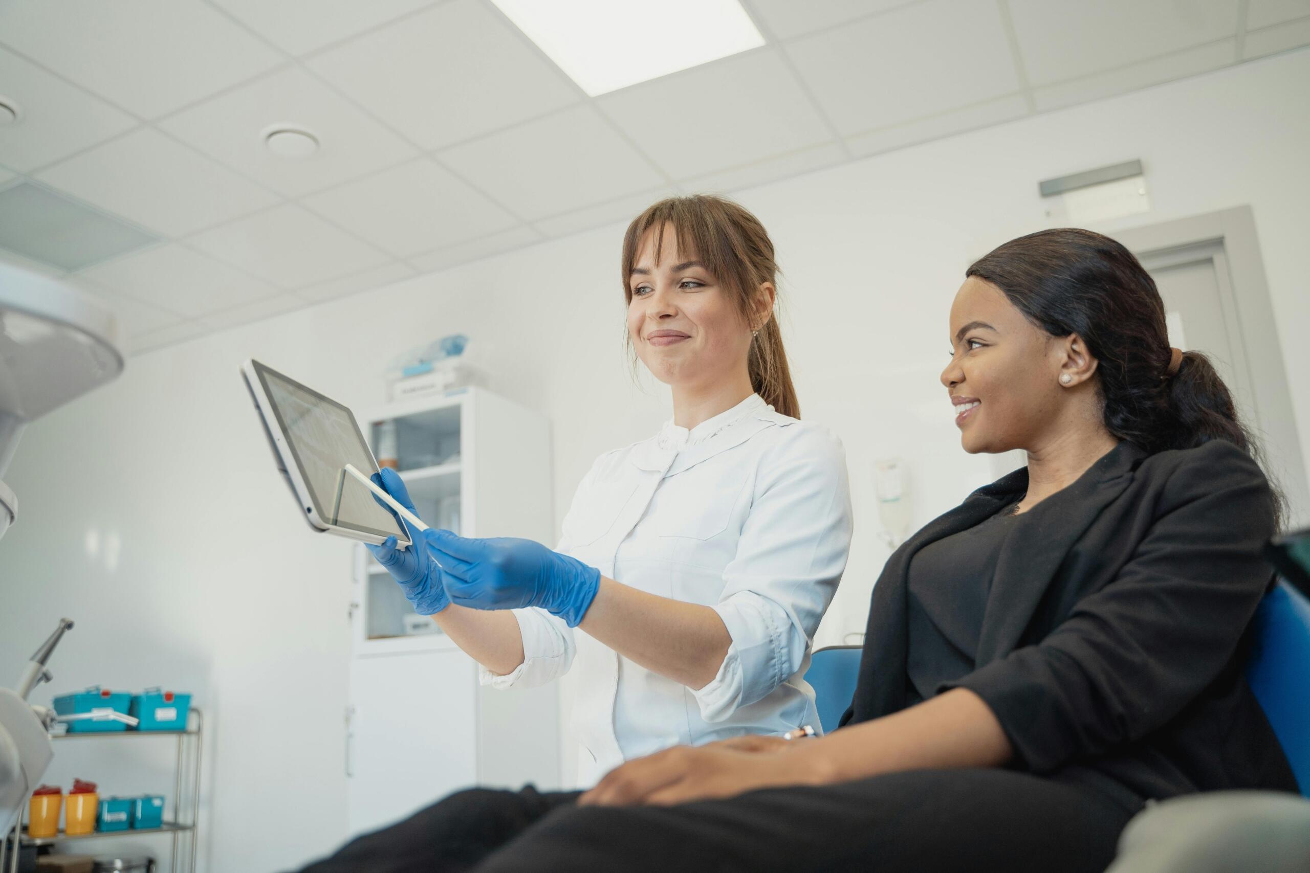 Smiling doctor in consultation rooms showing smiling patient information on an electronic tablet