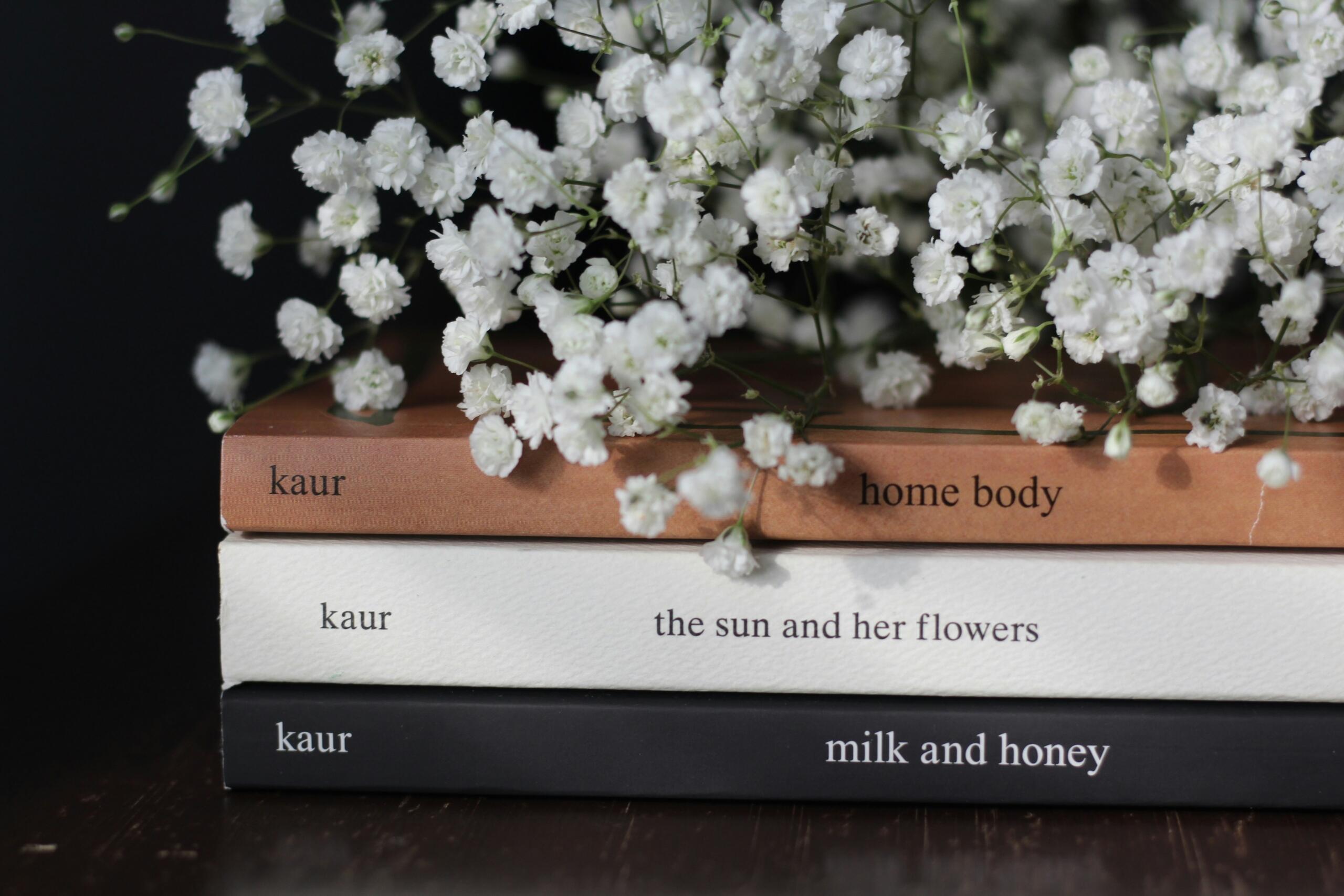 a pile of three poetry books piled with a bouquet of small white flowers on top