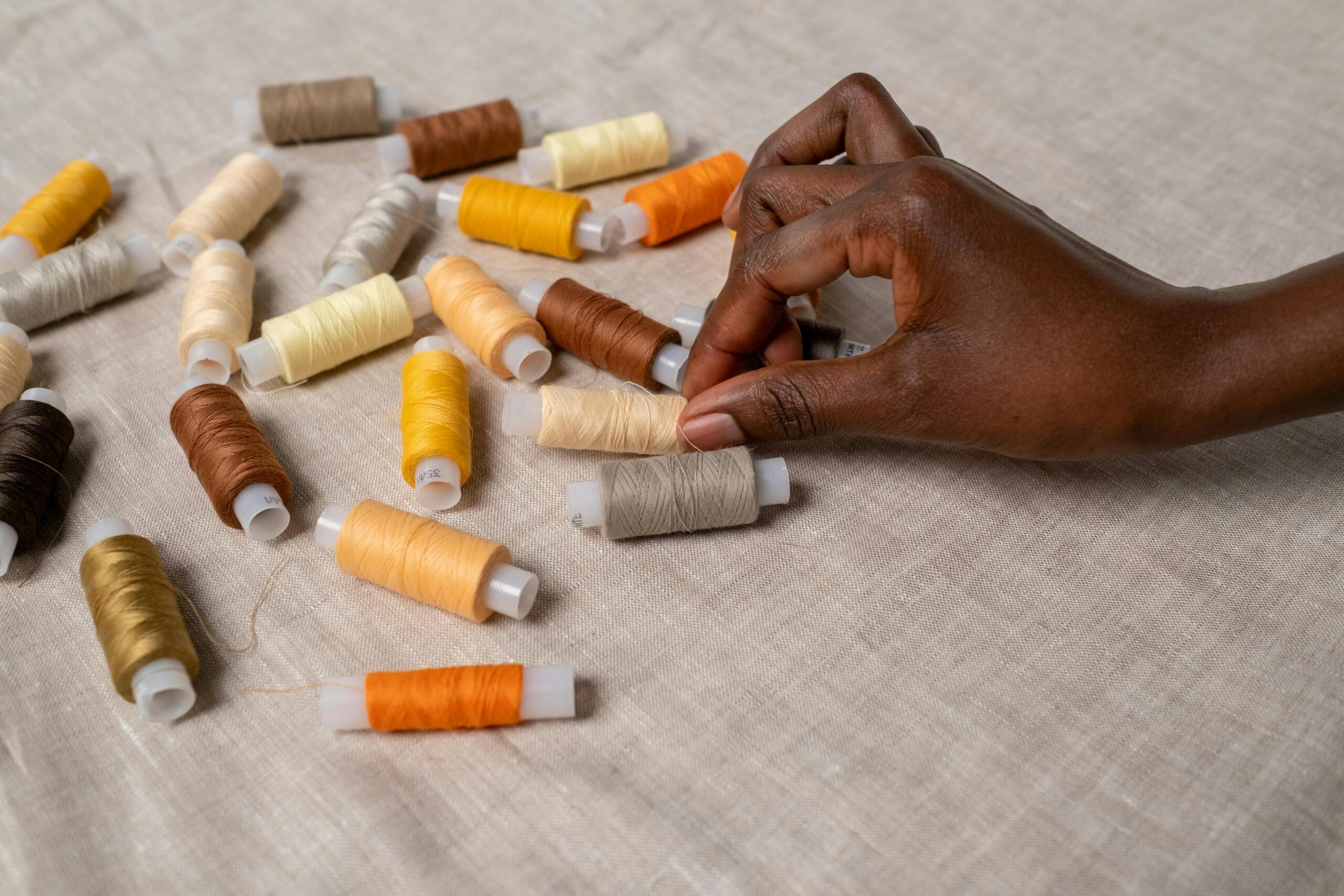 woman reaching for a roll of cotton thread from a collection of thread spools arranged on natural fabric