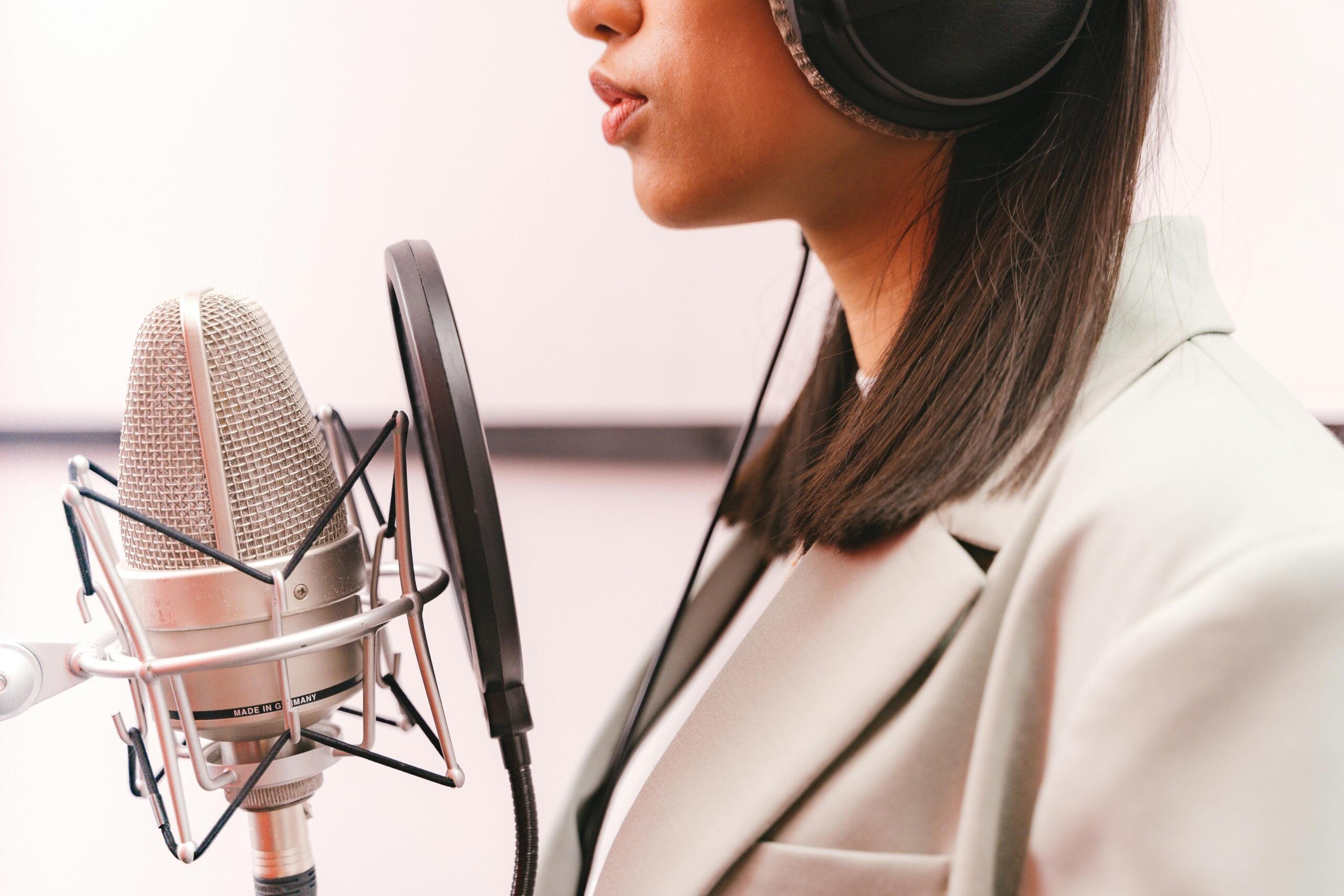 close up of a female singer standing in a recording studio behind a microphone wearing headphones