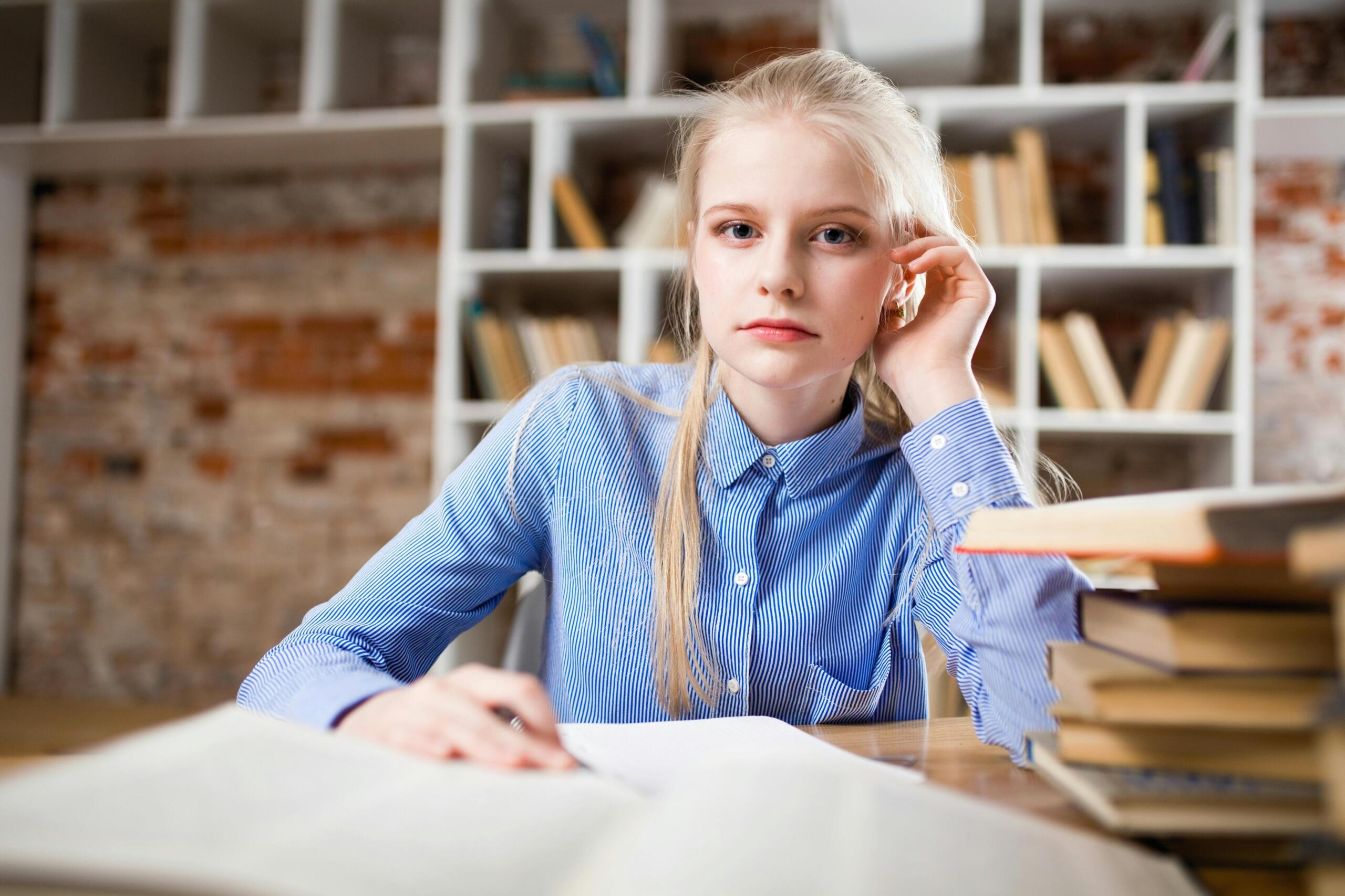student sitting at desk with a pile of books in the foreground while she makes notes