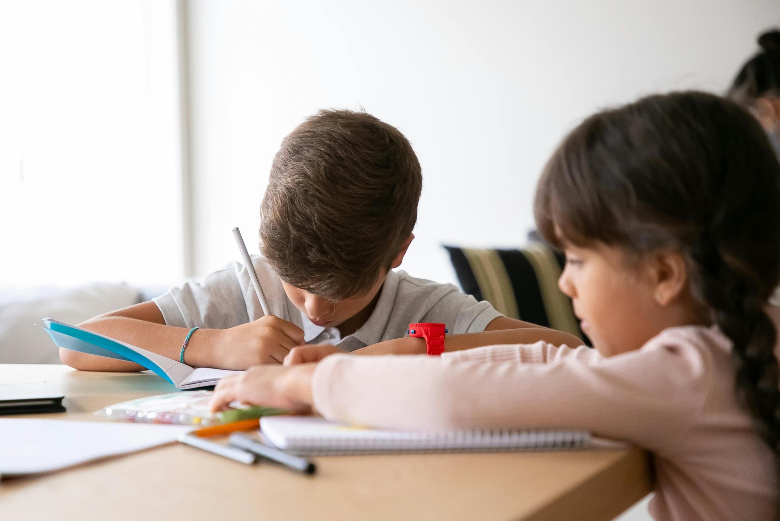 a boy and a girl sitting at a desk writing in lined notebooks