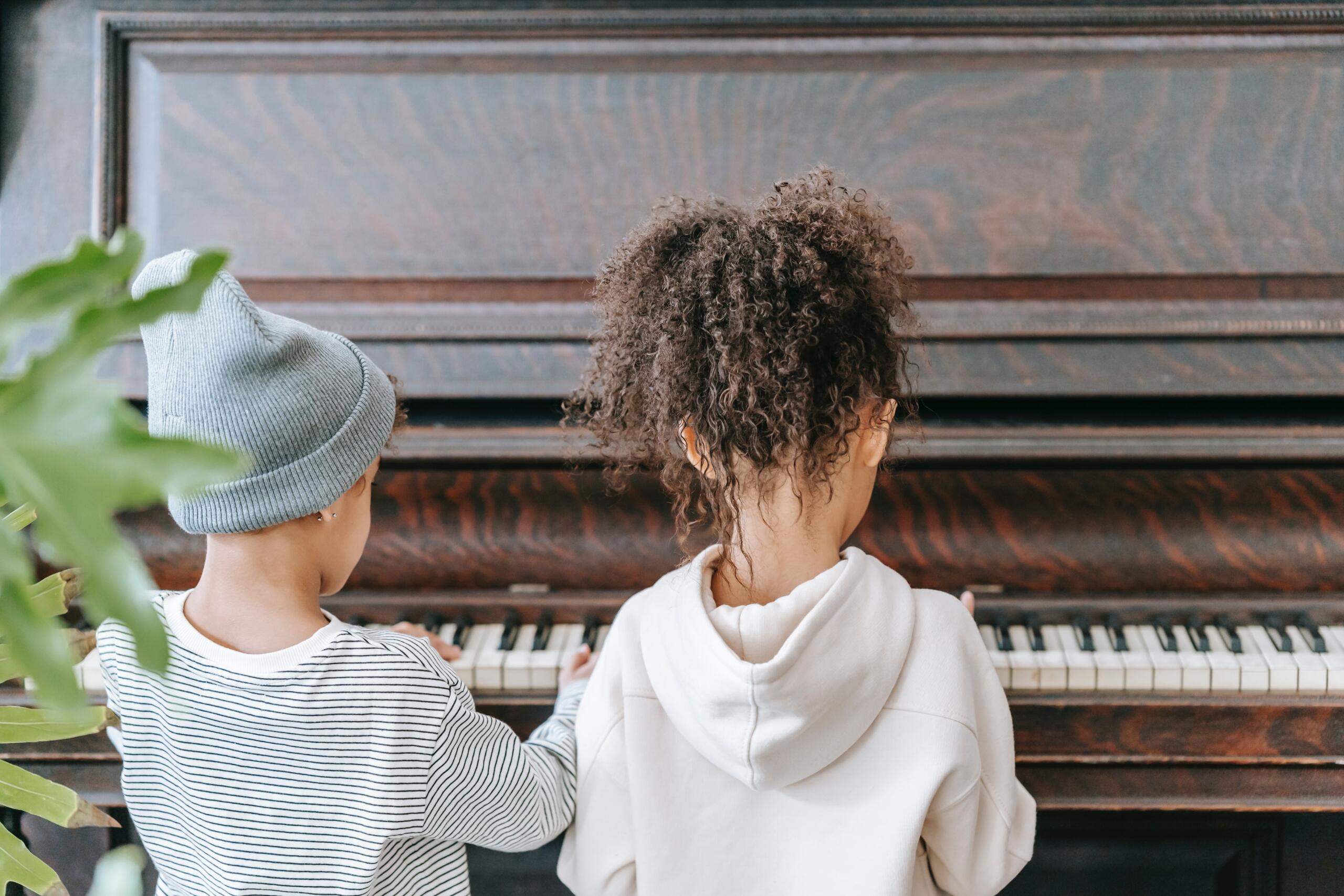 a young boy and girl sitting side by side on a piano stool in front of a brown piano