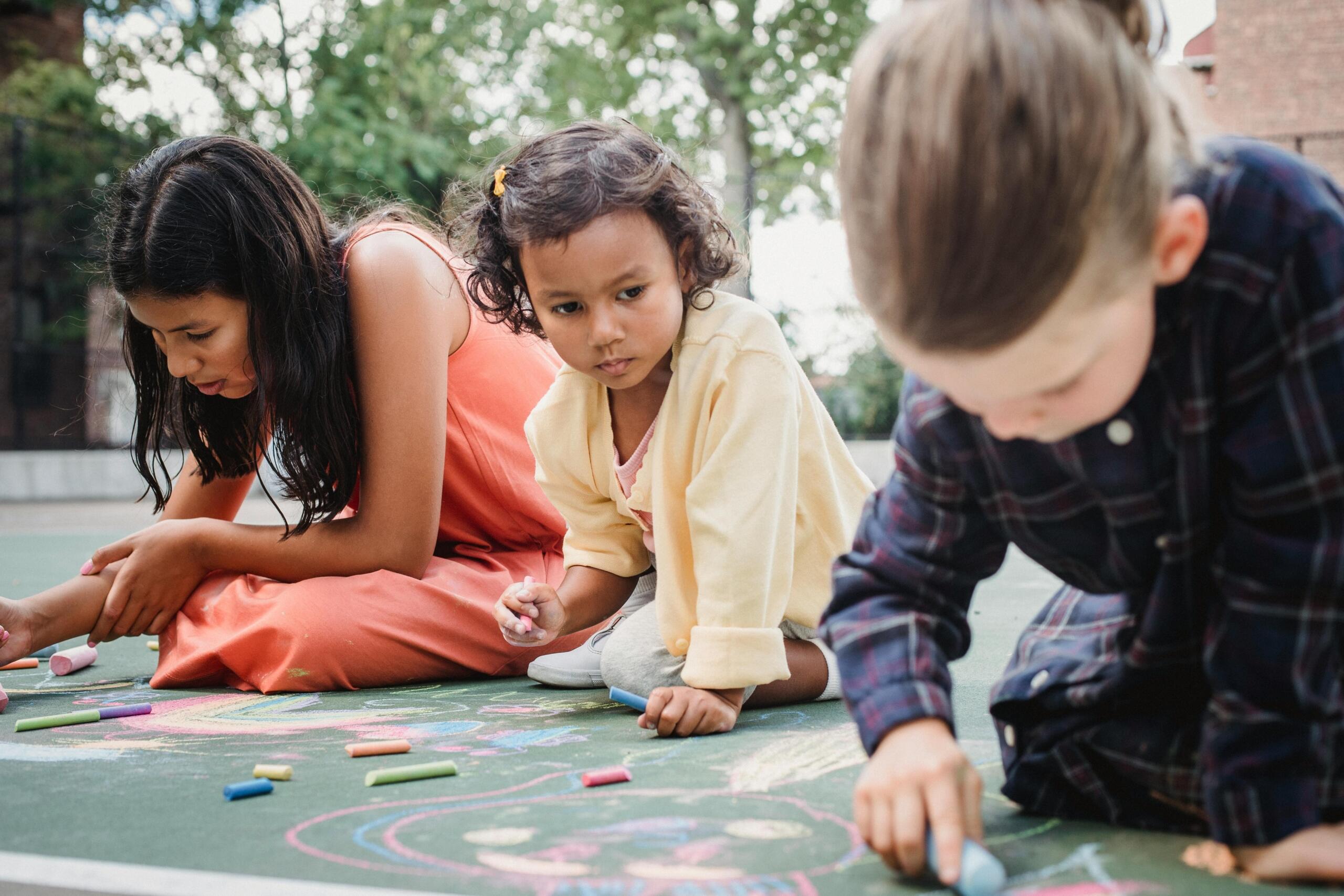 three girls drawing on an outside floor with colourful chalk
