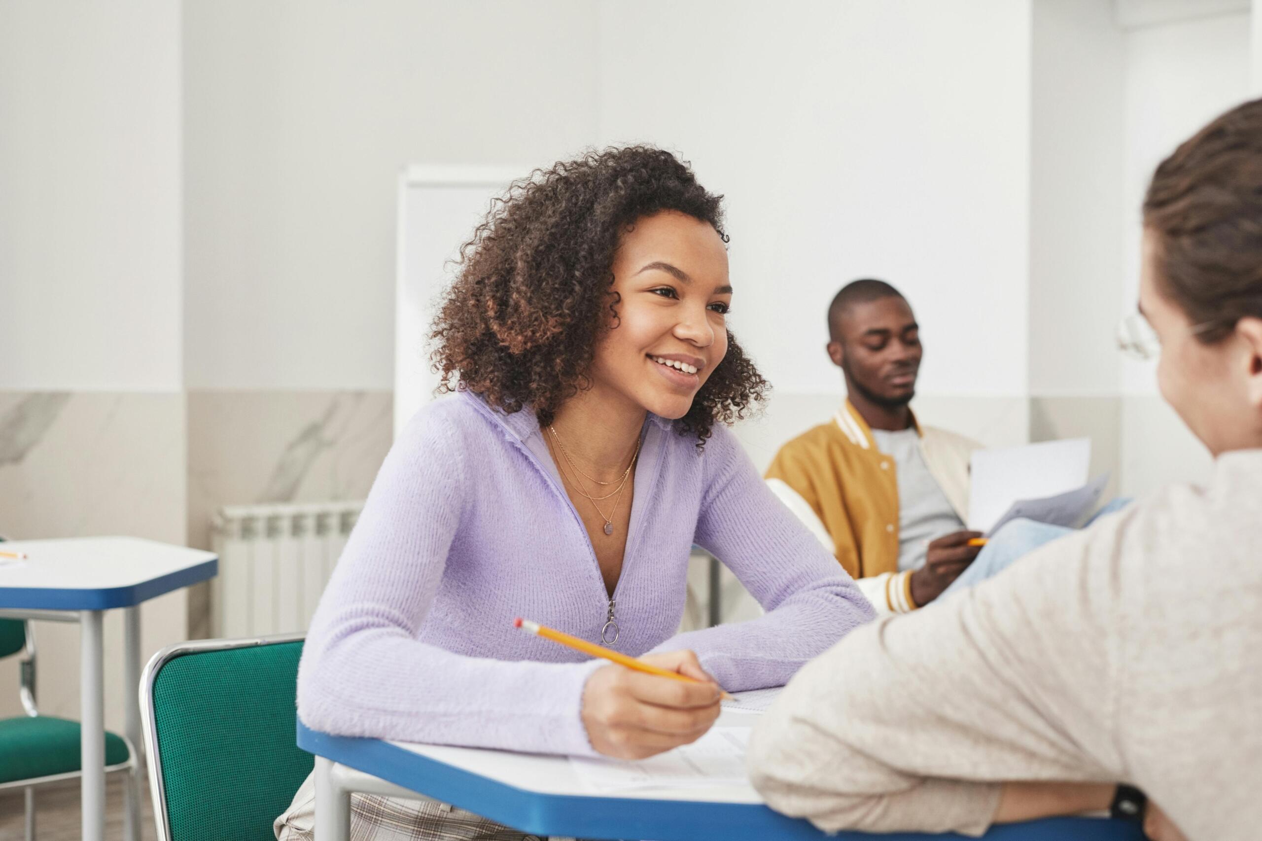 teen boy turning around and leaning on the desk of his female classmate to chat