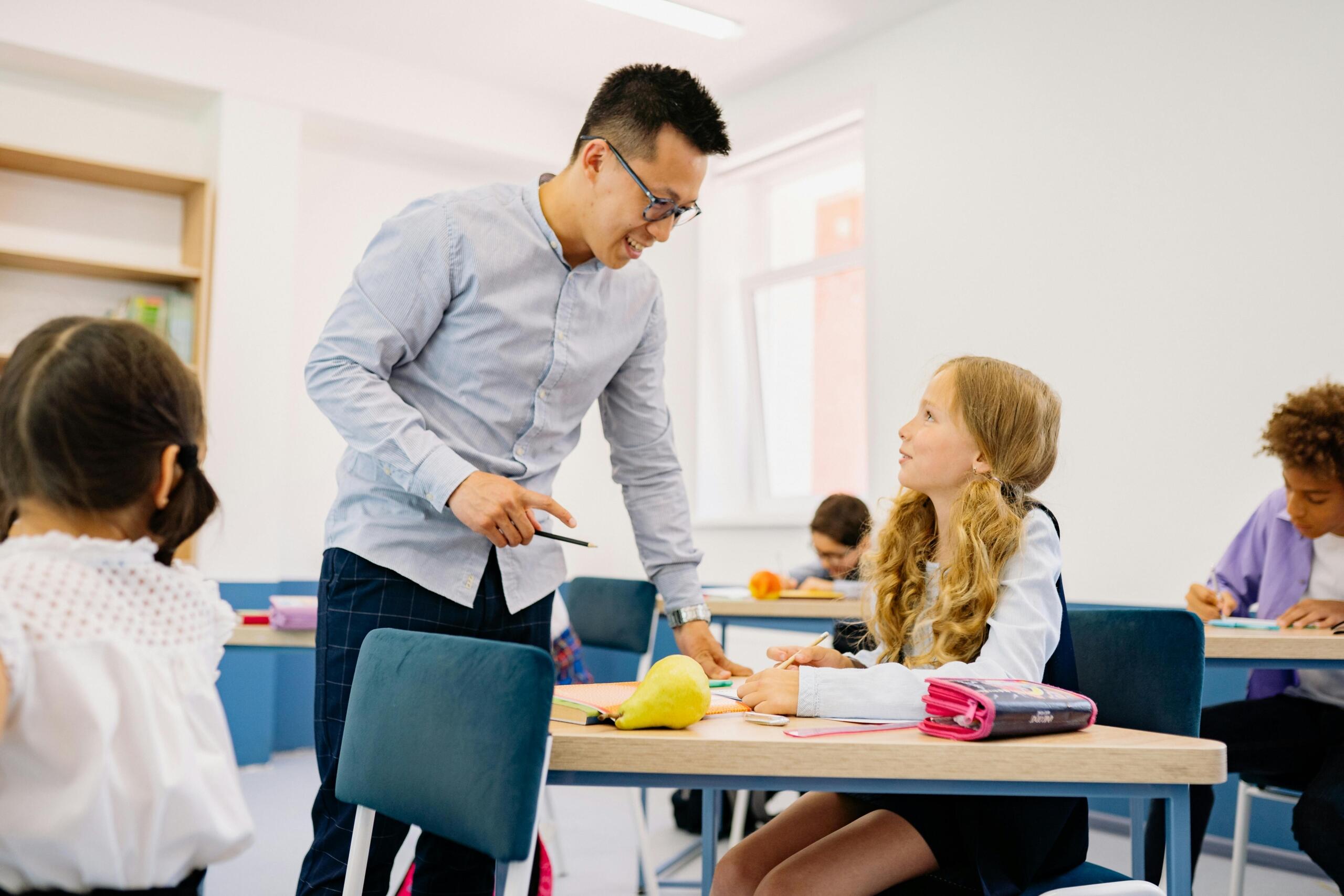 smiling teacher standing over the desk of student having a friendly chat