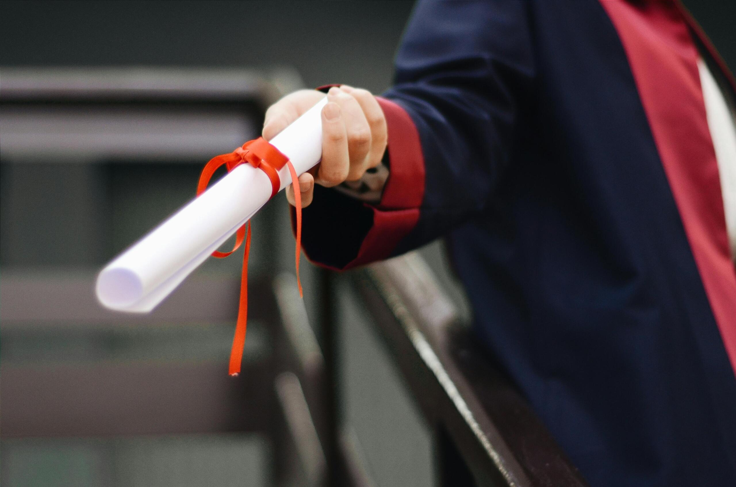 person holding out a diploma wrapped with a red ribbon