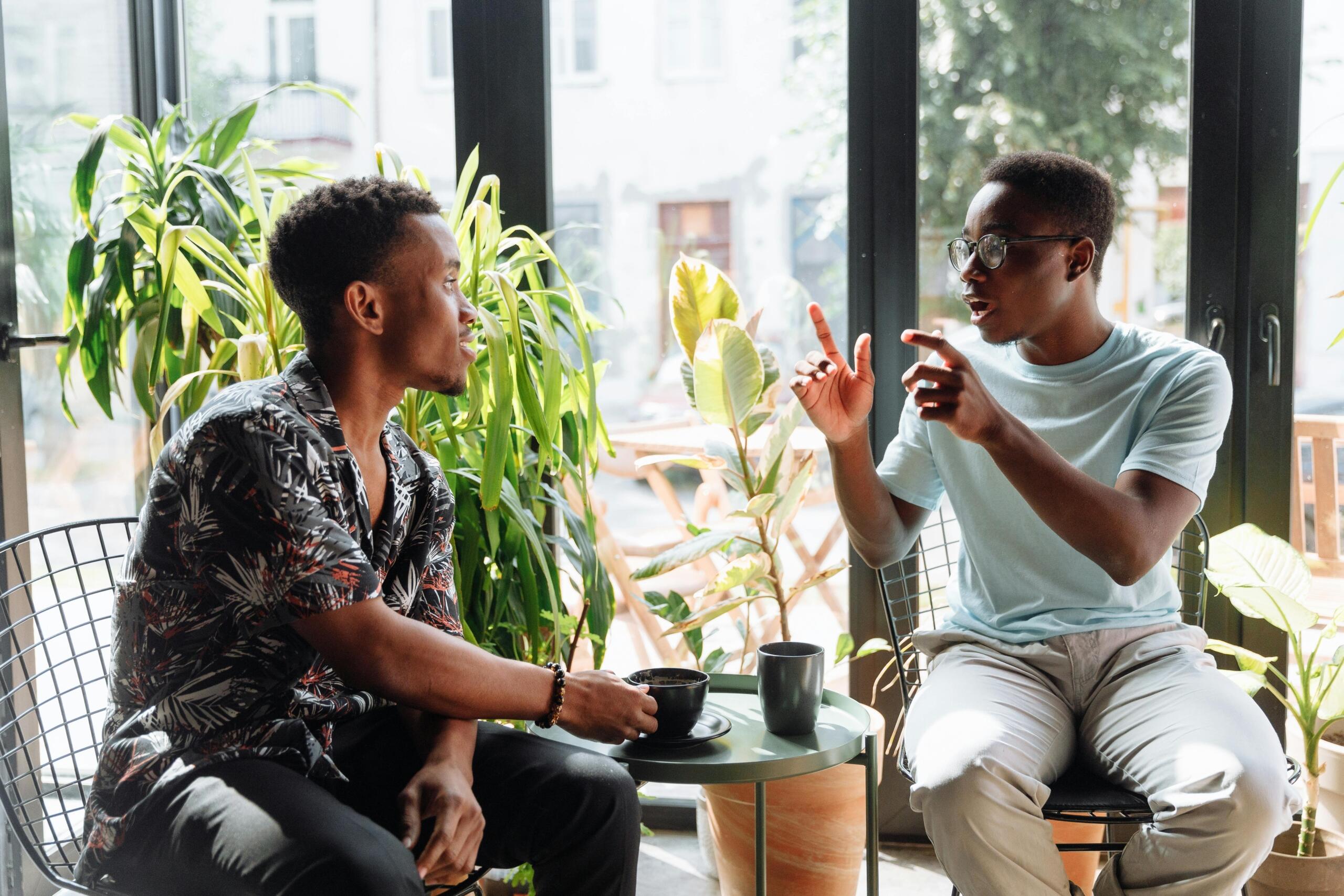 two men sitting side by side talking and drinking coffee