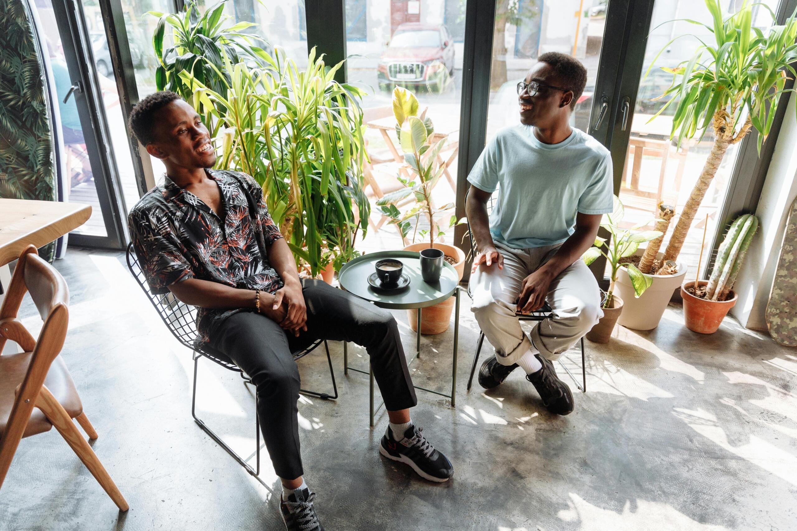 two smiling young men seated at a small coffee table having a discussion