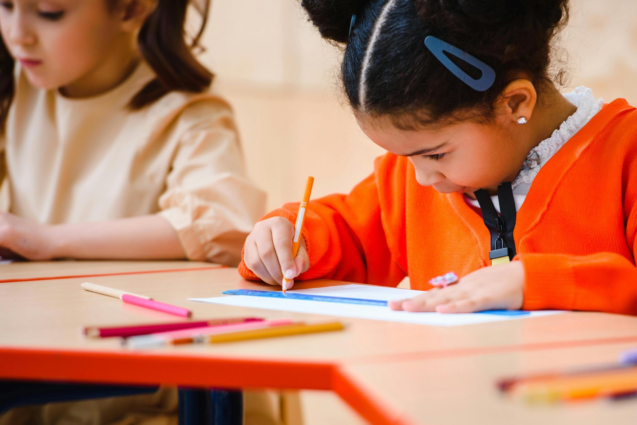 young girl sitting at a desk using a ruler and coloured pencil