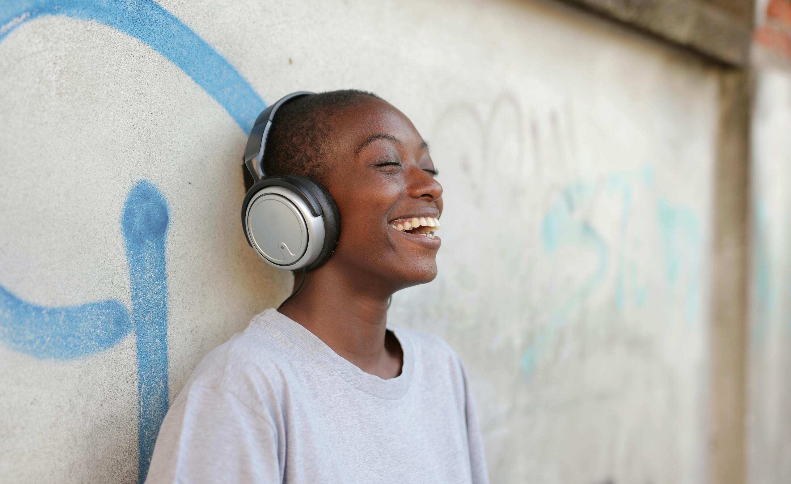laughing woman wearing headphones and standing with her back to a wall