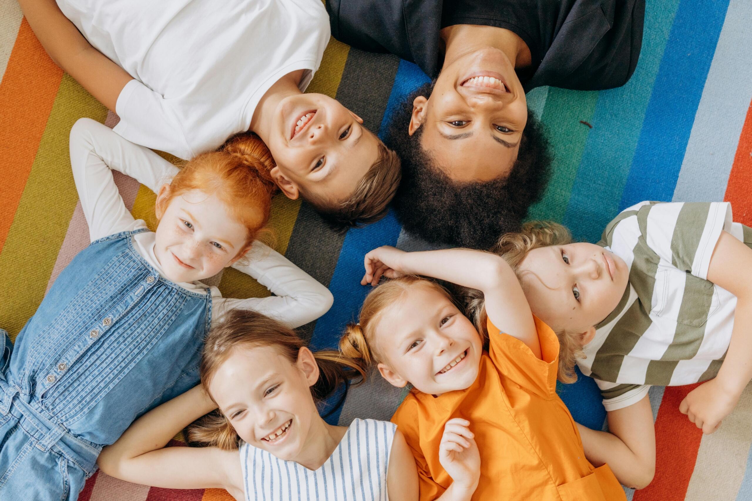 a group of smiling young children lying on the ground in a circle with their teacher