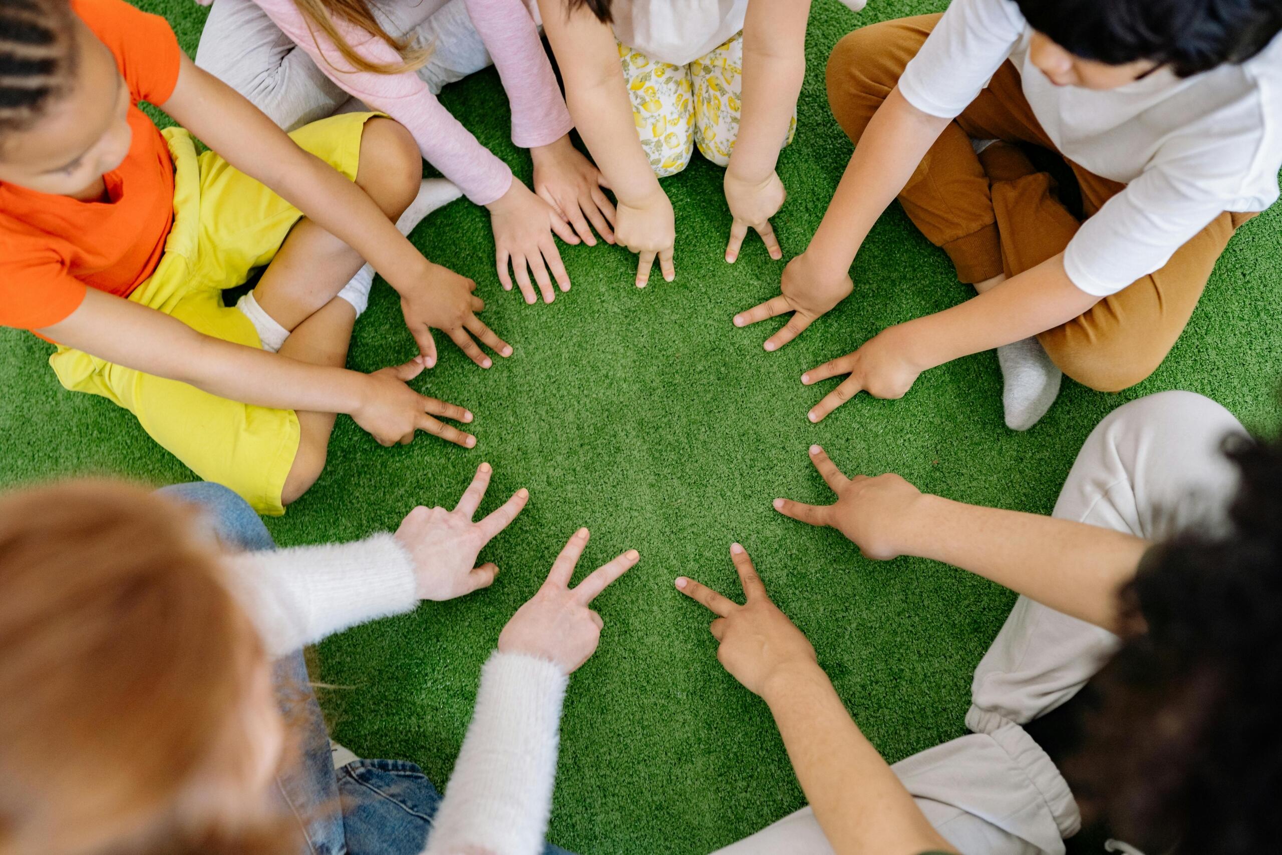 a group of young children sitting on the ground in a circle holding out their fingers in front of themselves