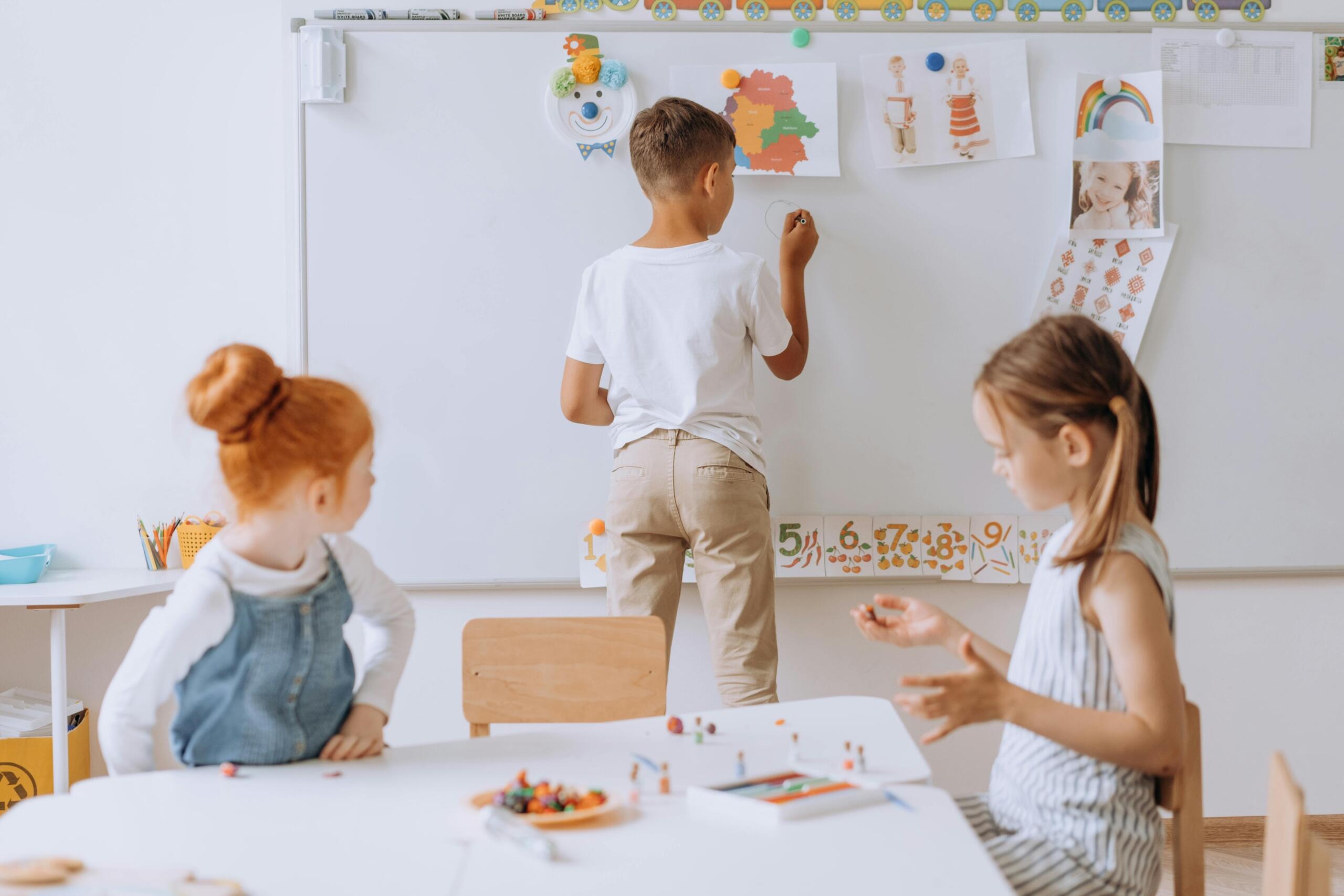 boy writing on whiteboard in classroom while two classmates look on
