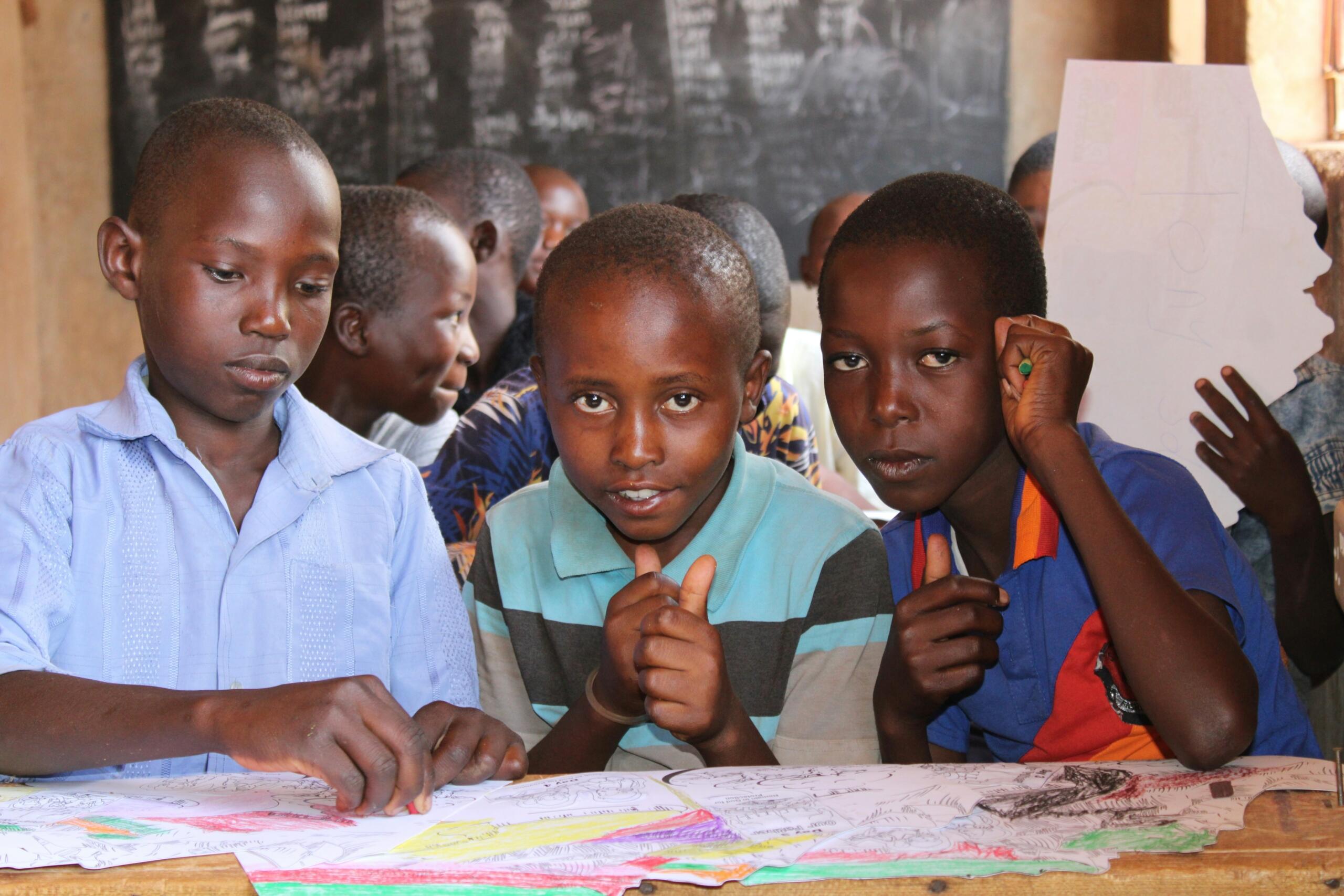 three boys in a classroom working on pieces of paper