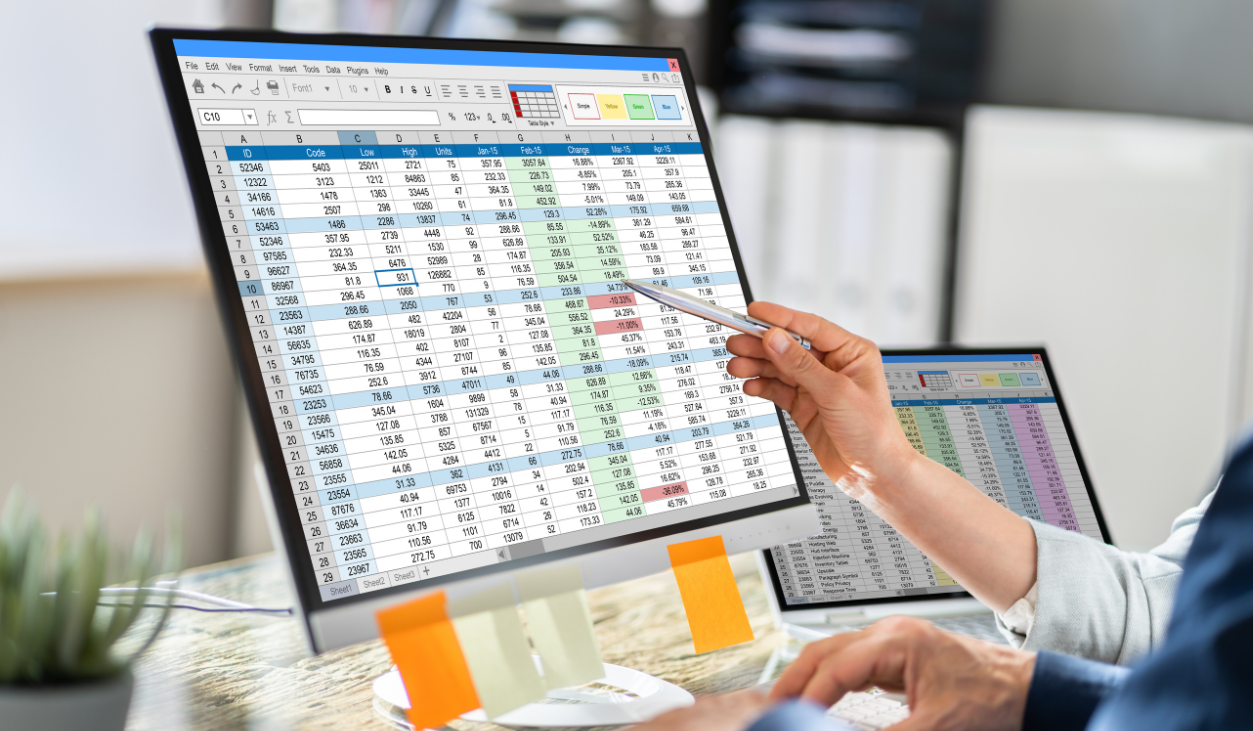 people looking at Microsoft Excel spreadsheet on a computer monitor next to a laptop