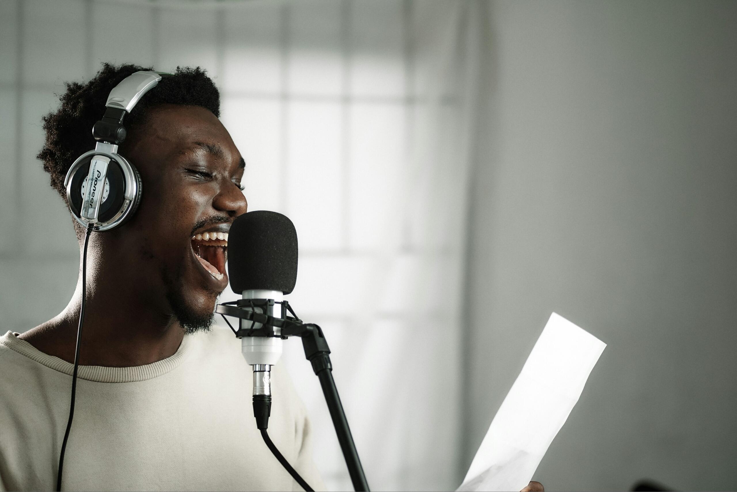 person wearing headphones singing into a microphone and reading lyrics from a sheet of paper