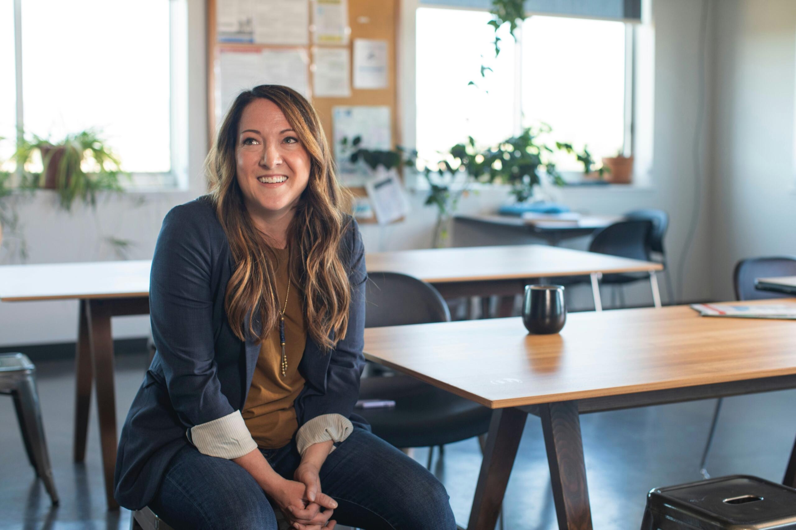 a smiling woman sitting on a chair in an empty classroom