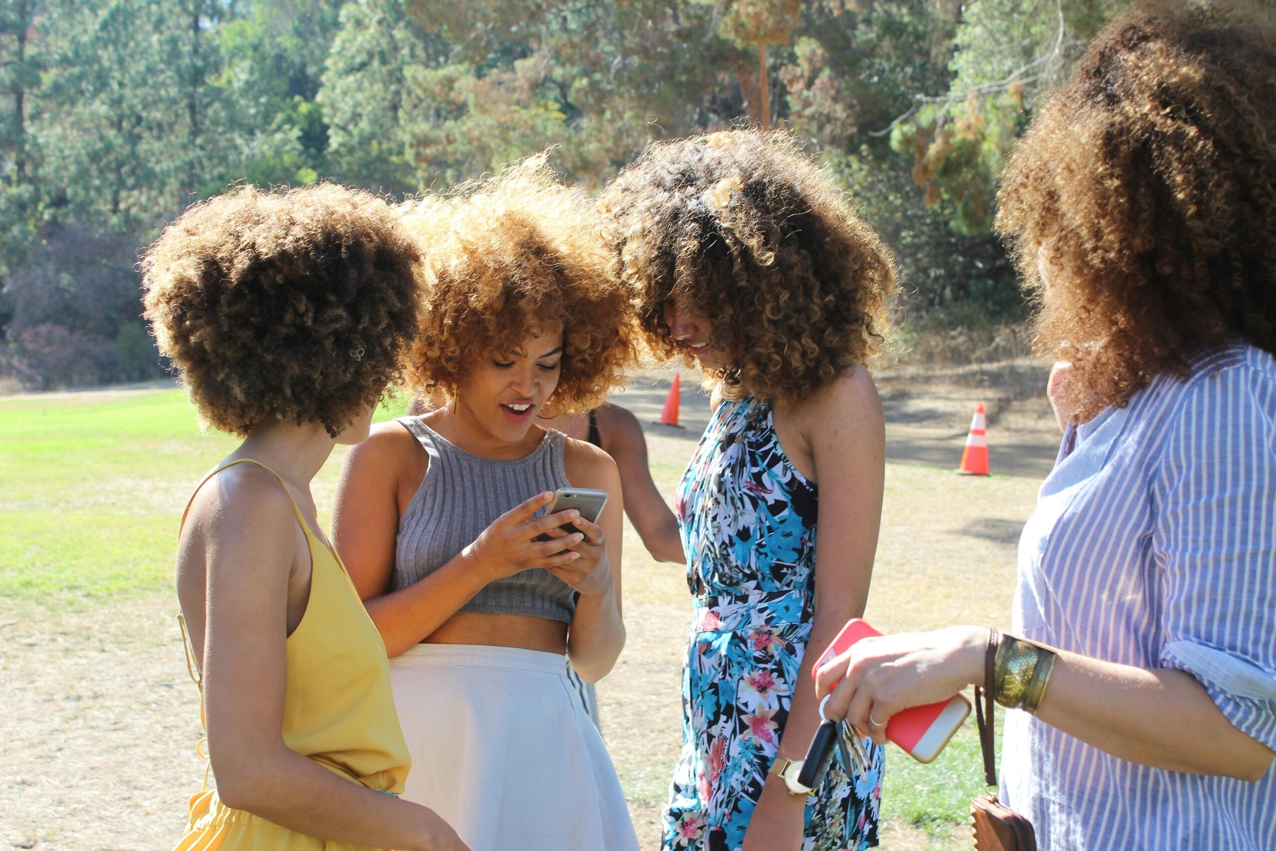 group of women standing around outside looking at one mobile phone