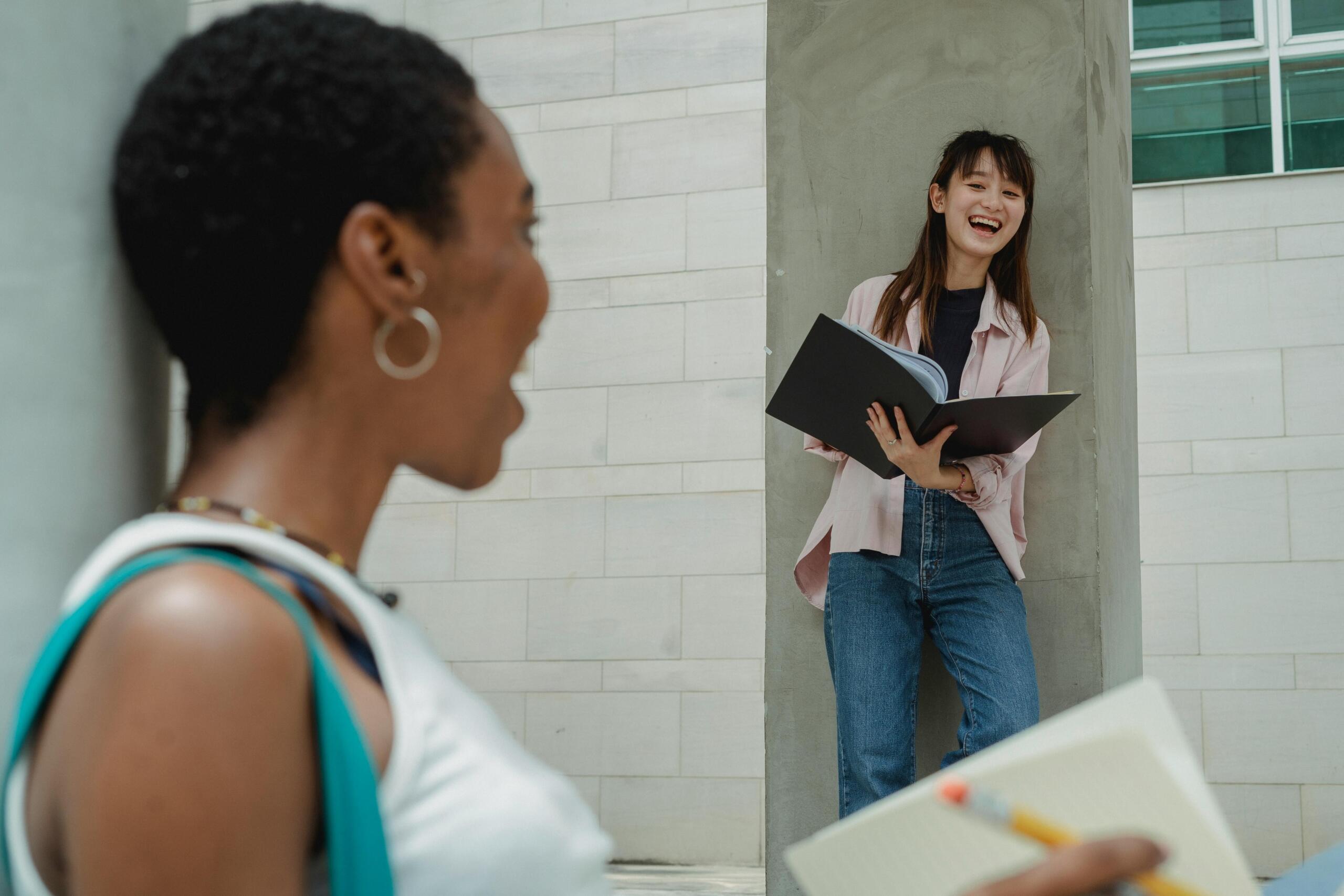 one student standing while the other sits, both laughing and holding notes