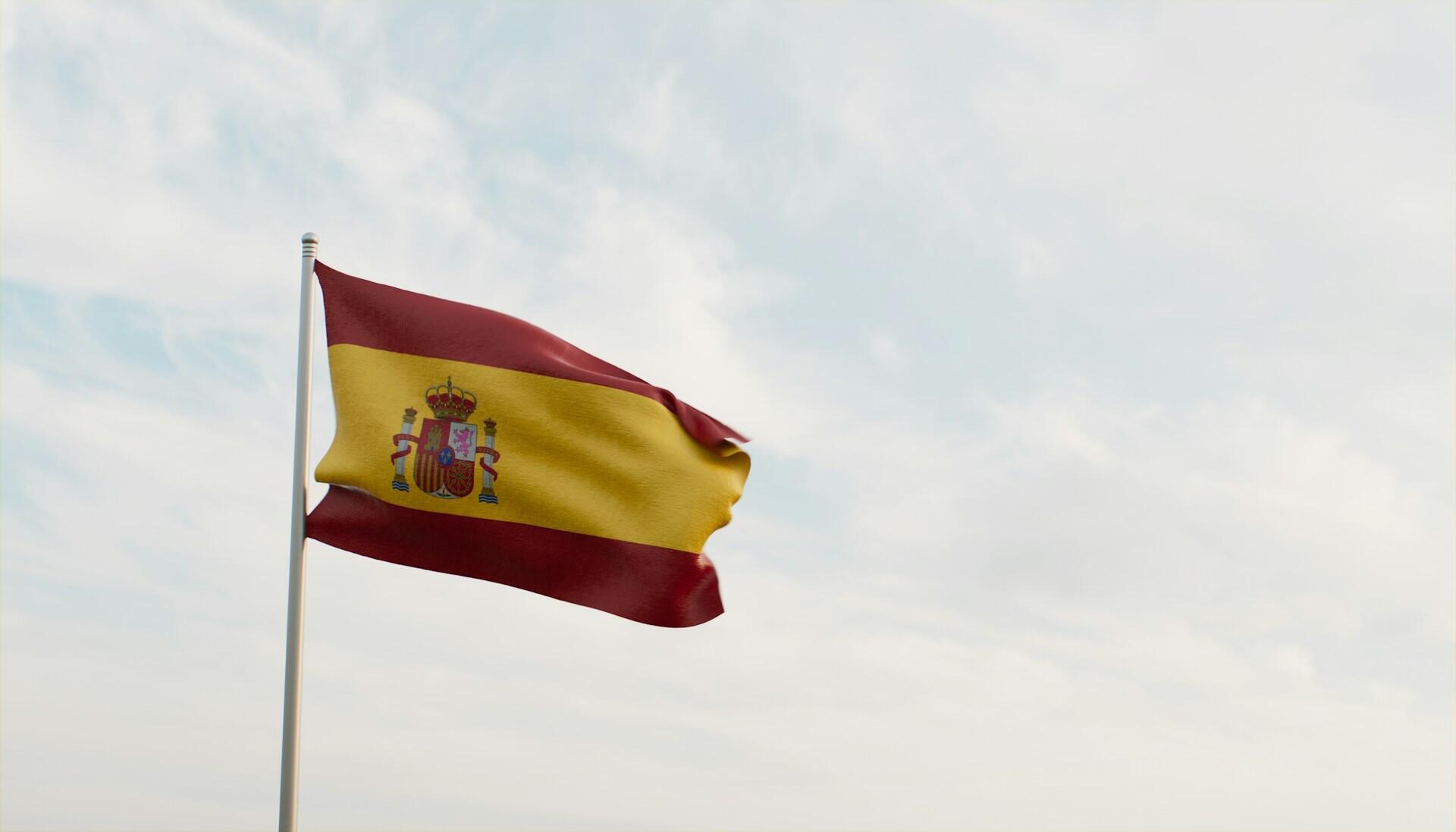 Spanish flag on a flag pole fluttering against backdrop of a partly cloudy sky