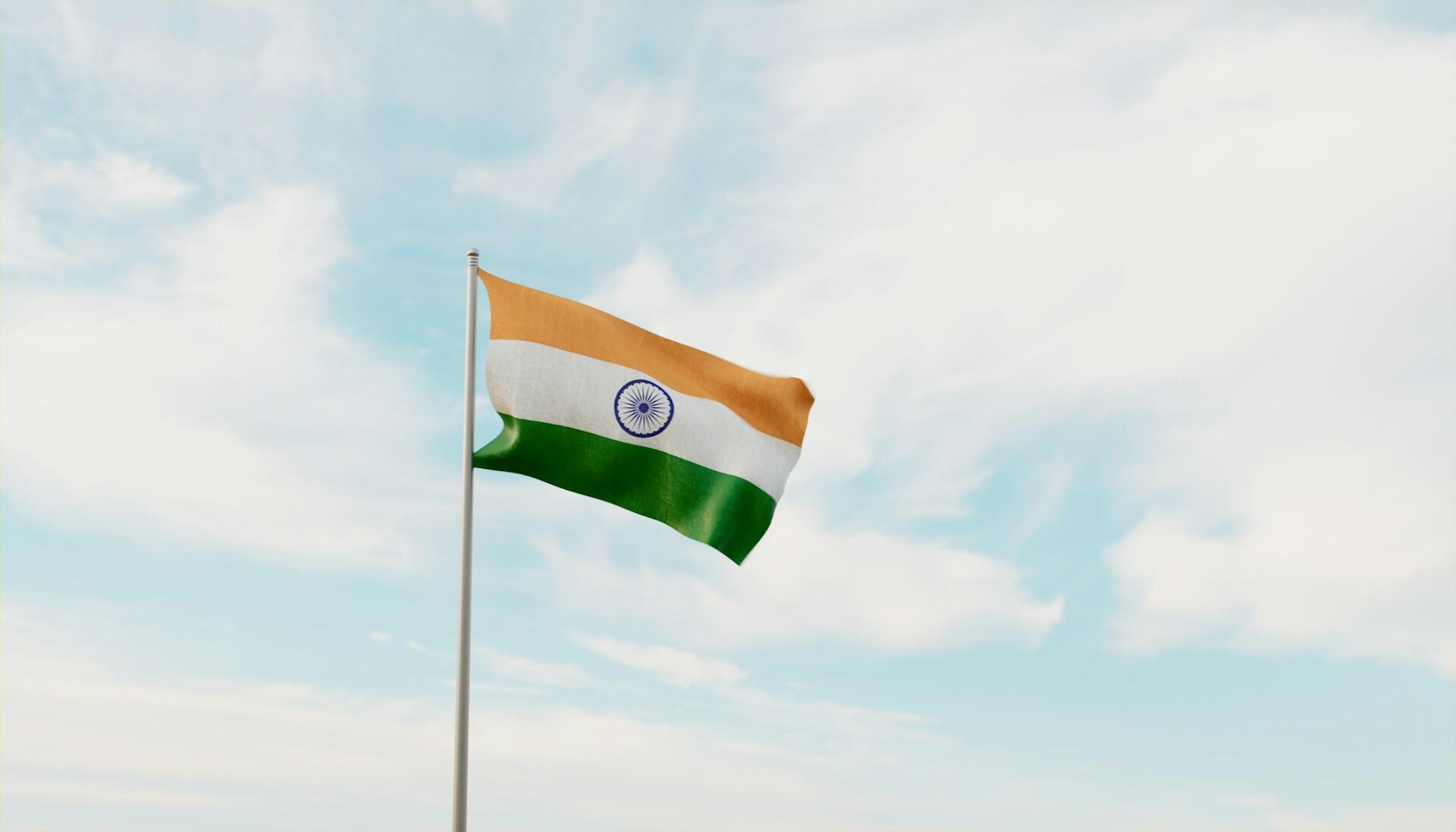 Flag of India on a flag pole fluttering against backdrop of a partly cloudy sky