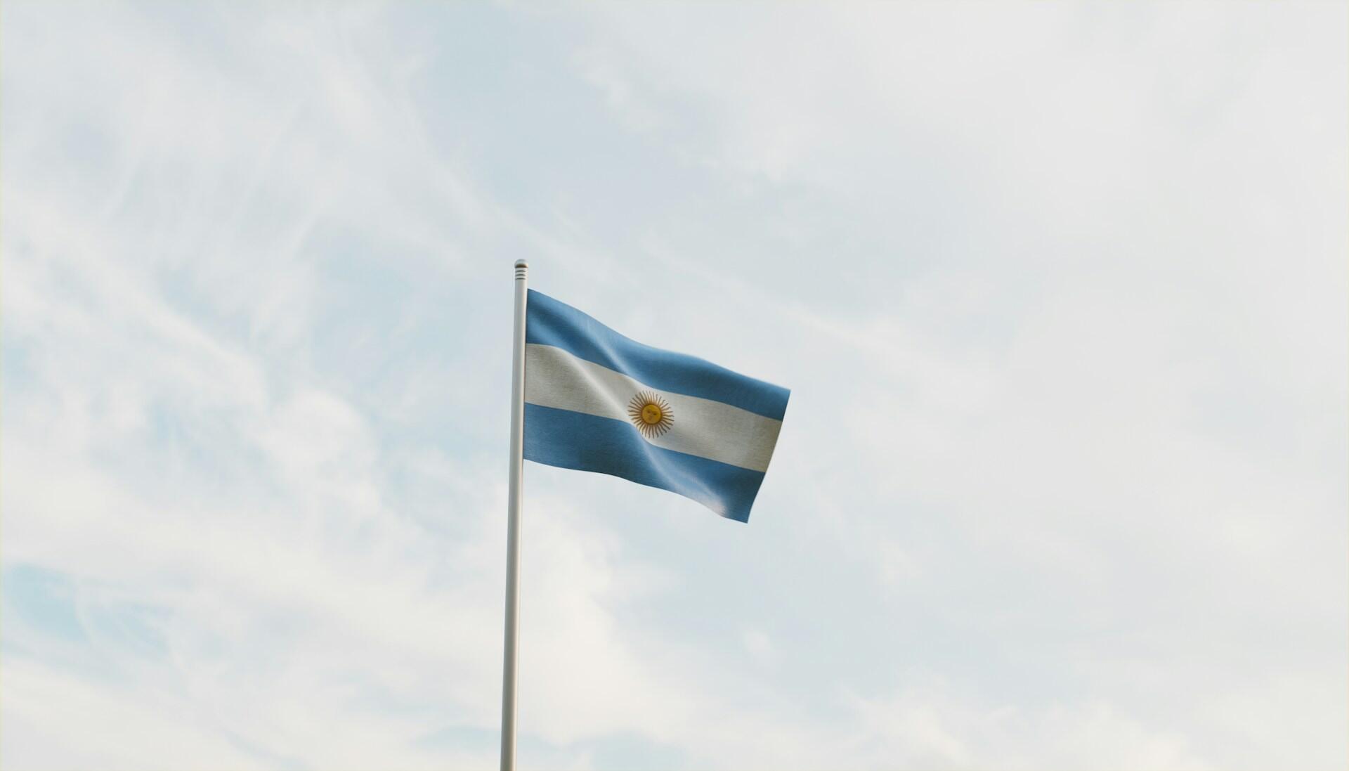 Argentinian flag on a flag pole fluttering against backdrop of a partly cloudy sky