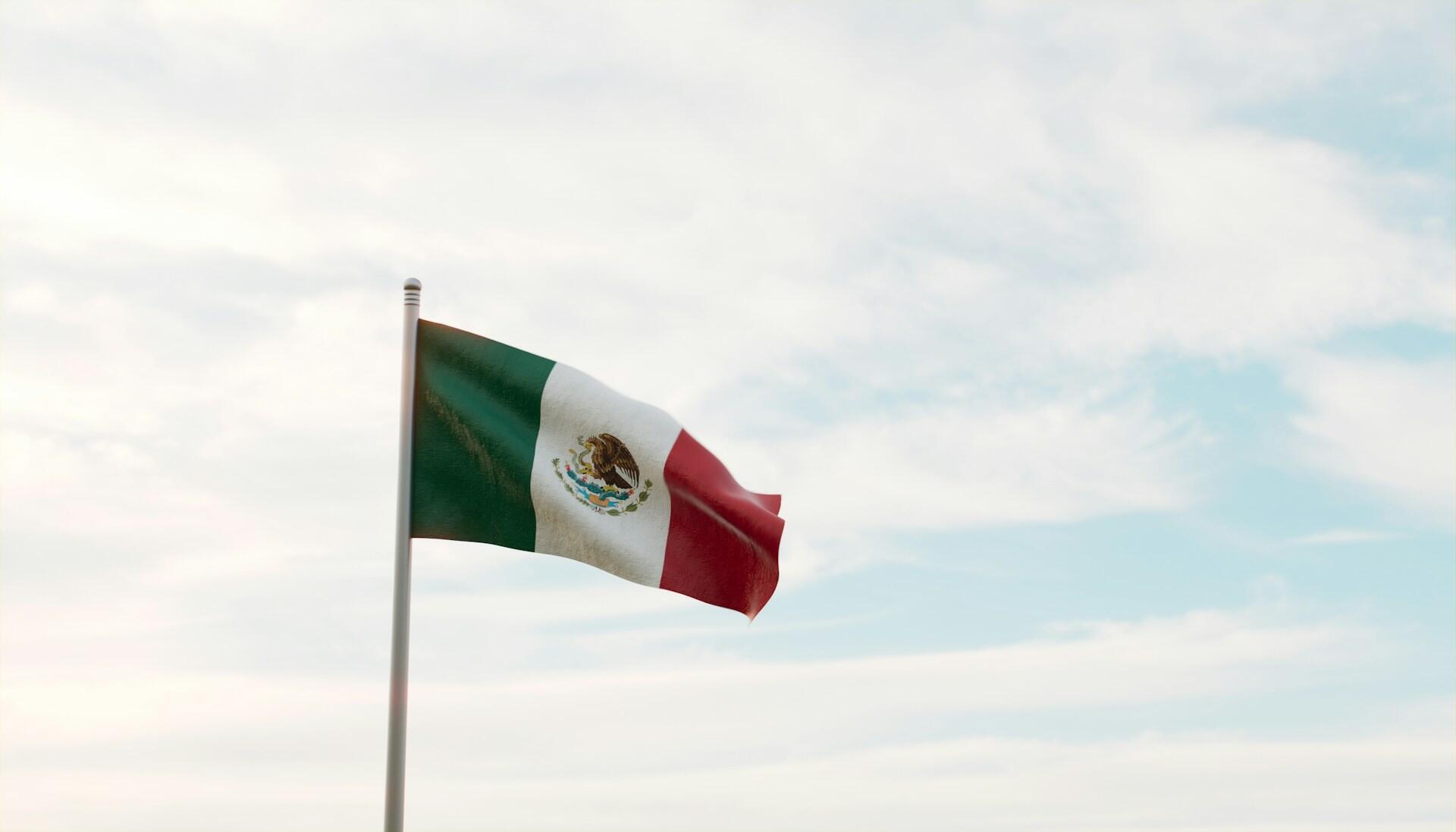 Mexican flag flag on a flag pole fluttering against backdrop of a partly cloudy sky