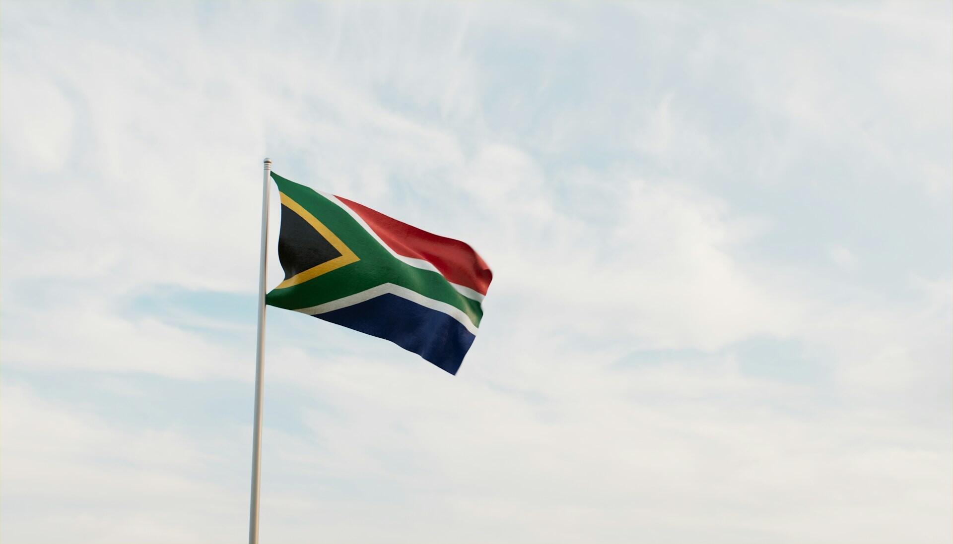 South African flag on a flag pole fluttering against backdrop of a partly cloudy sky