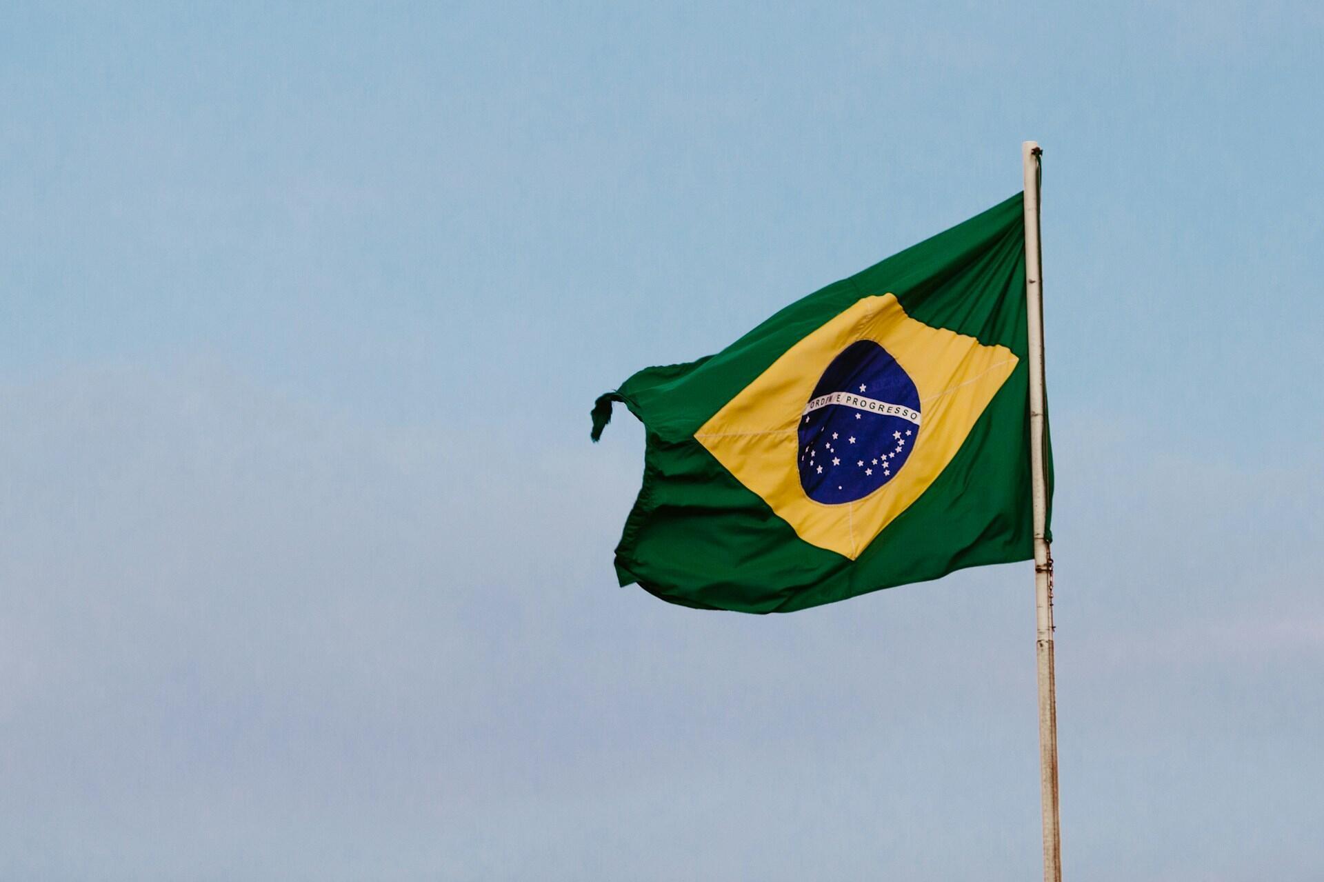 Brazilian flag on a flag pole fluttering against backdrop of a partly cloudy sky