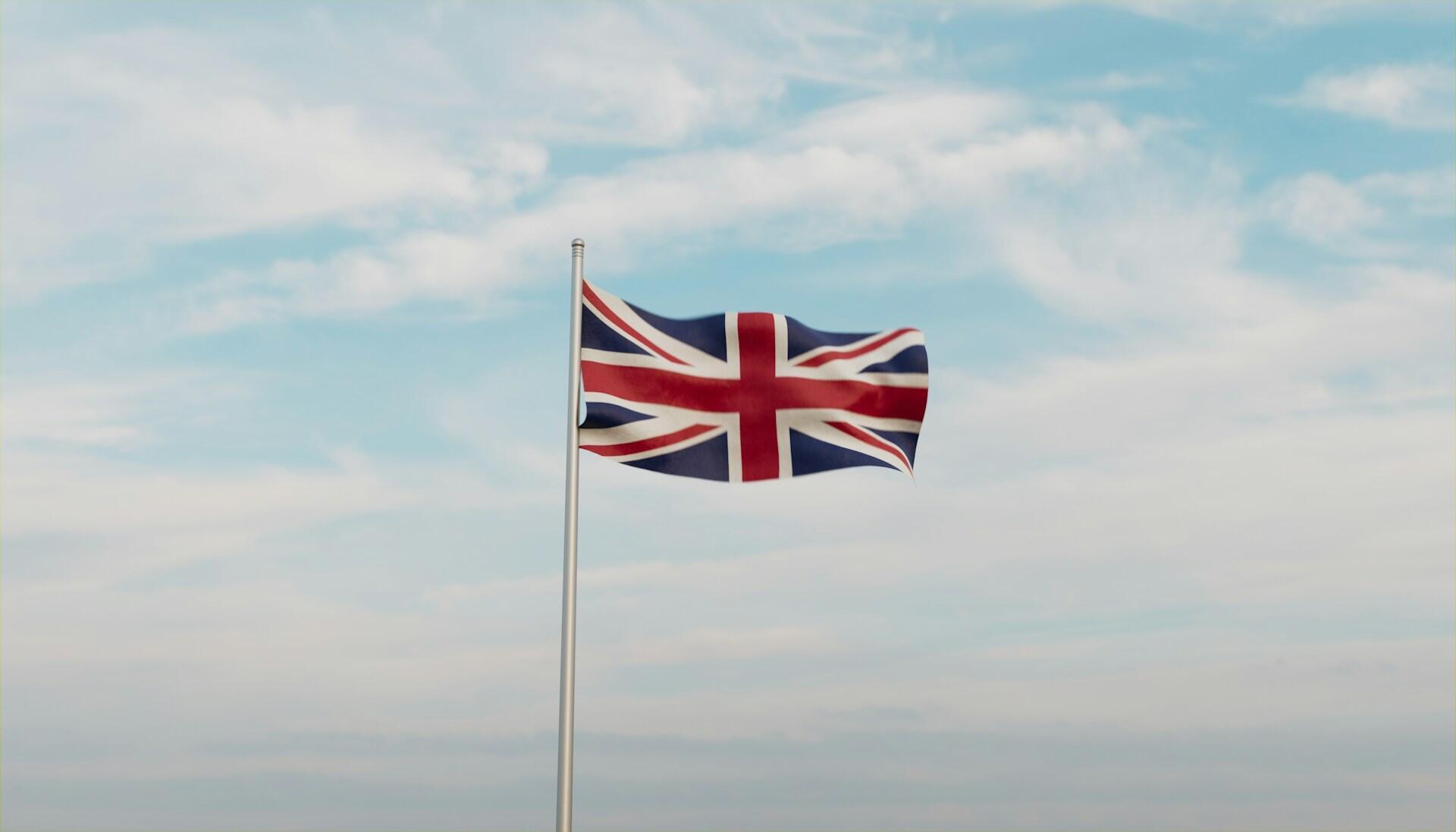 UK flag on a flag pole fluttering against backdrop of a partly cloudy sky