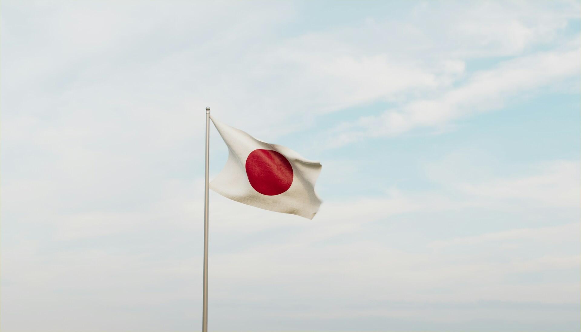 Japanese flag on a flag pole fluttering against backdrop of a partly cloudy sky