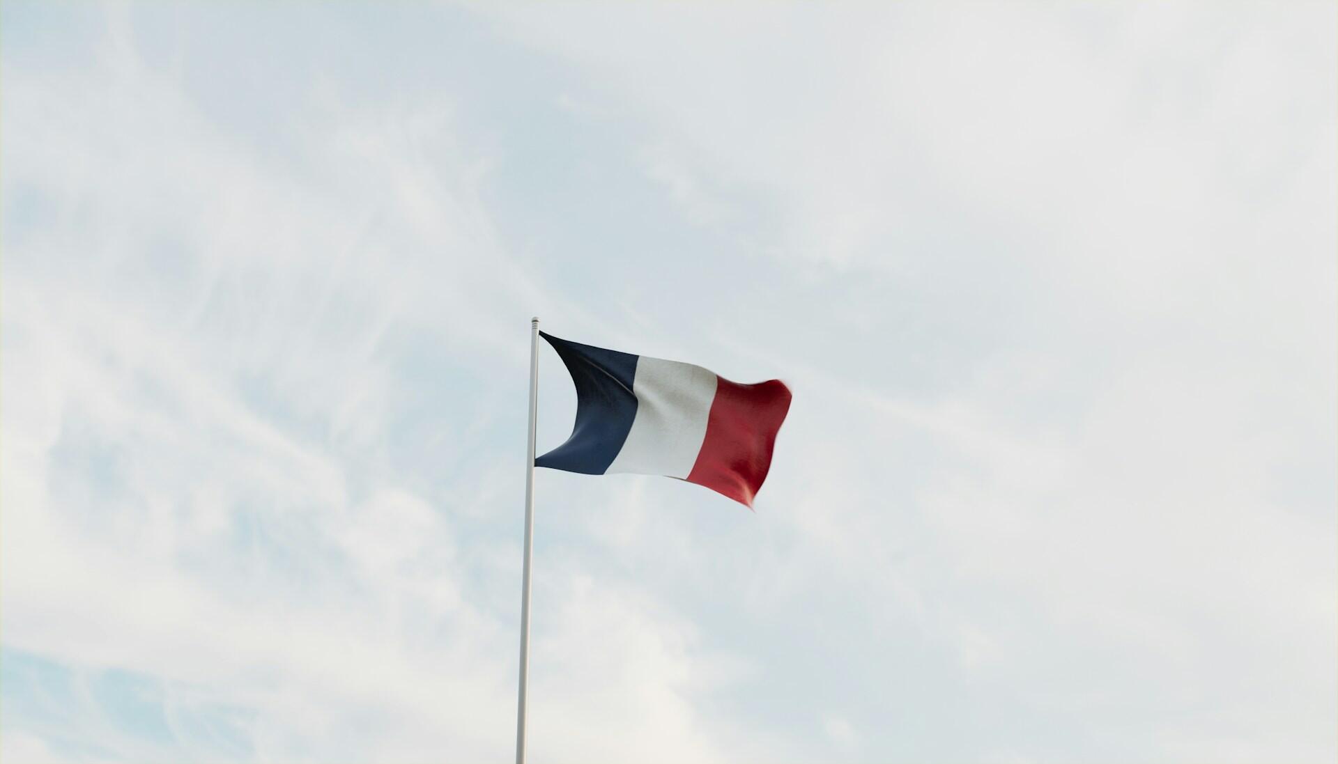 French flag on a flag pole fluttering against backdrop of a partly cloudy sky