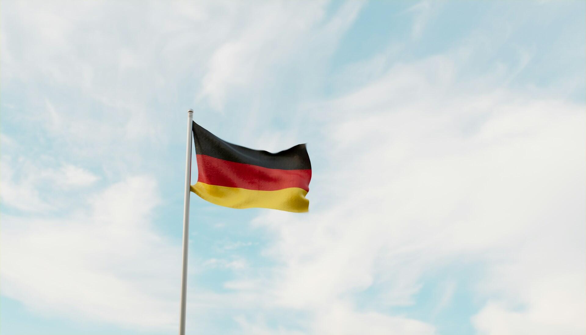 German flag on a flag pole fluttering against backdrop of a partly cloudy sky