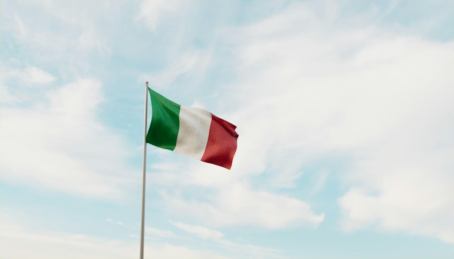Italian flag on a flag pole fluttering against backdrop of a partly cloudy sky