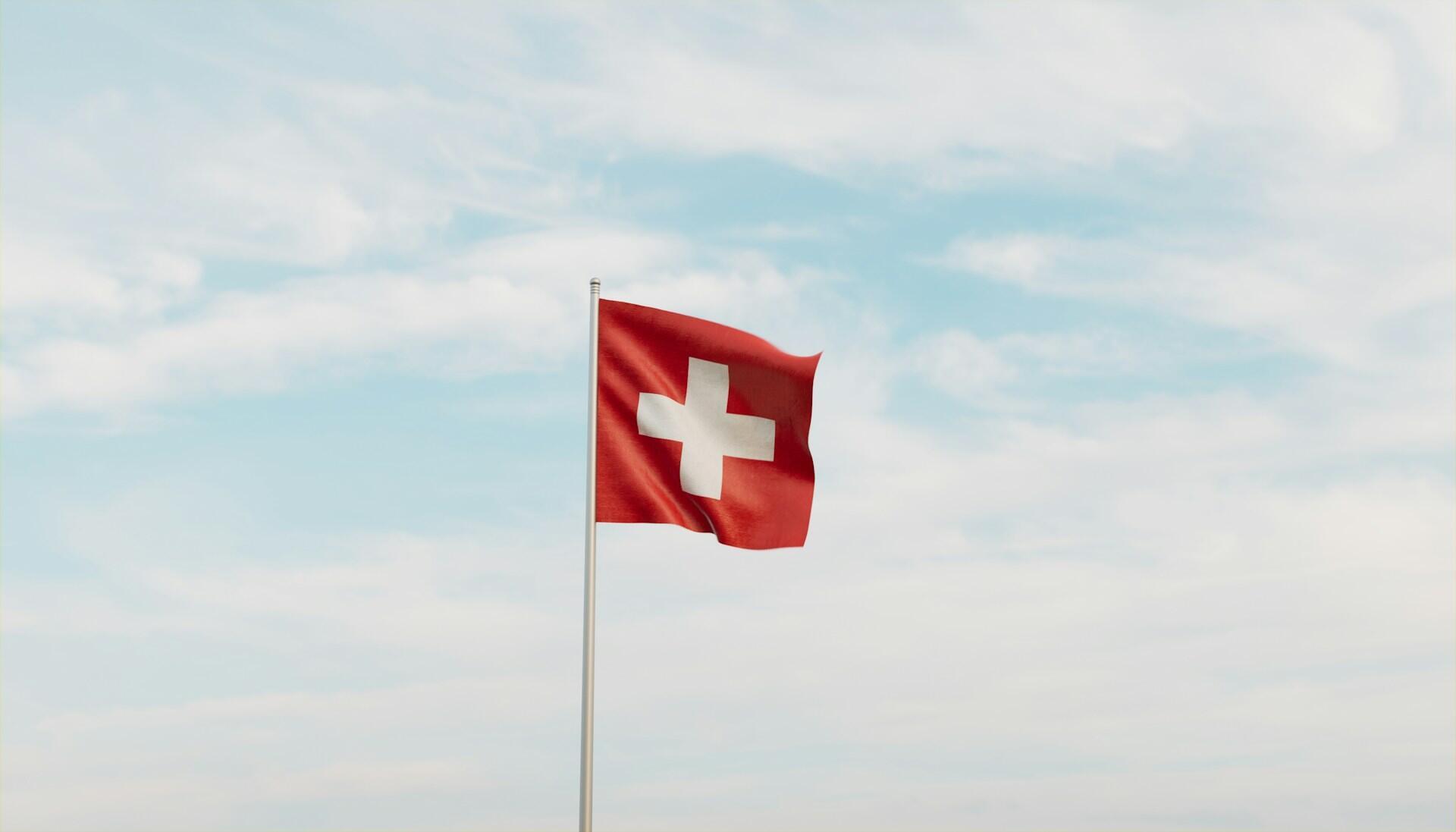 Swiss flag on a flag pole fluttering against backdrop of a partly cloudy sky