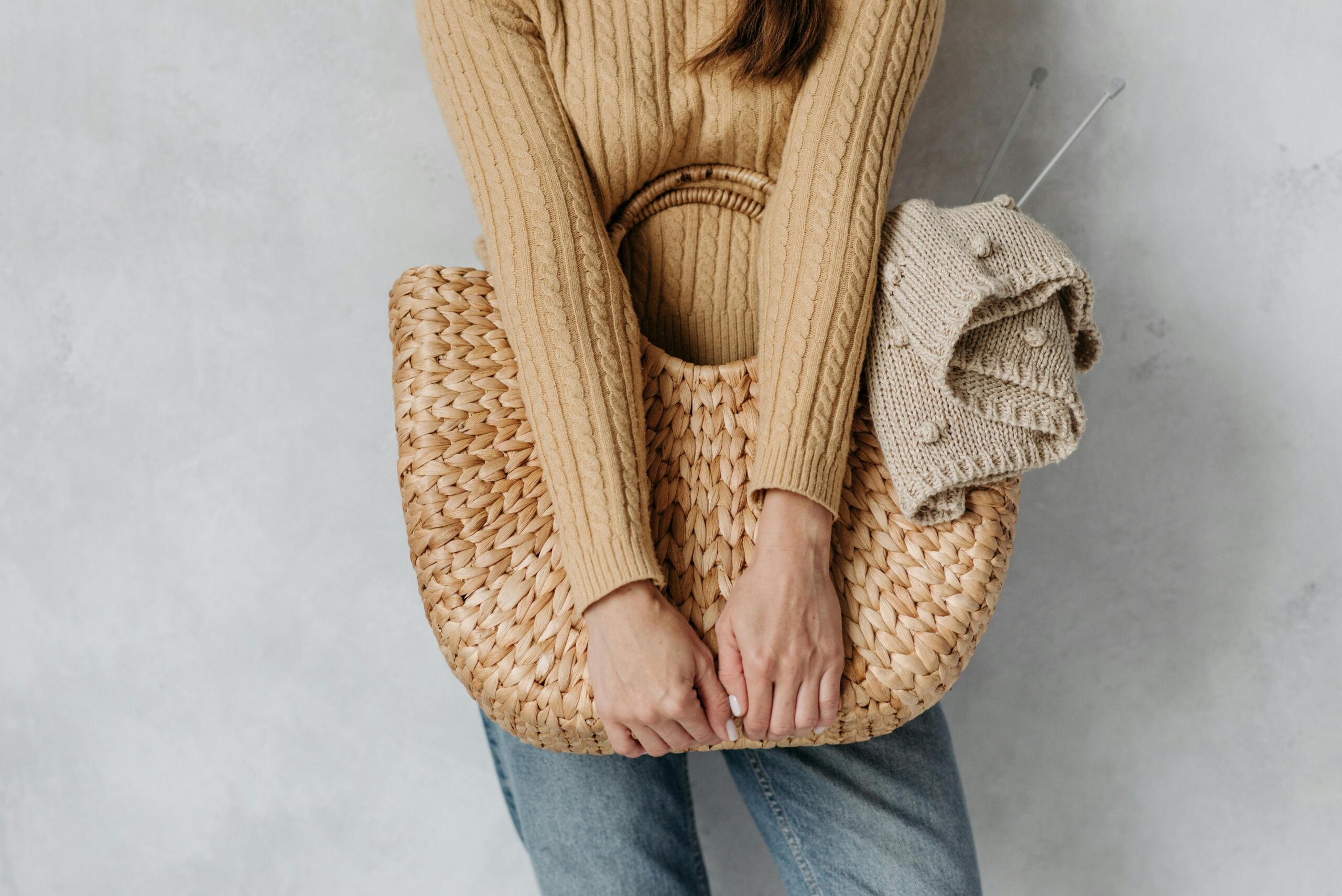 woman holding a woven bag containing knitting project and knitting needles
